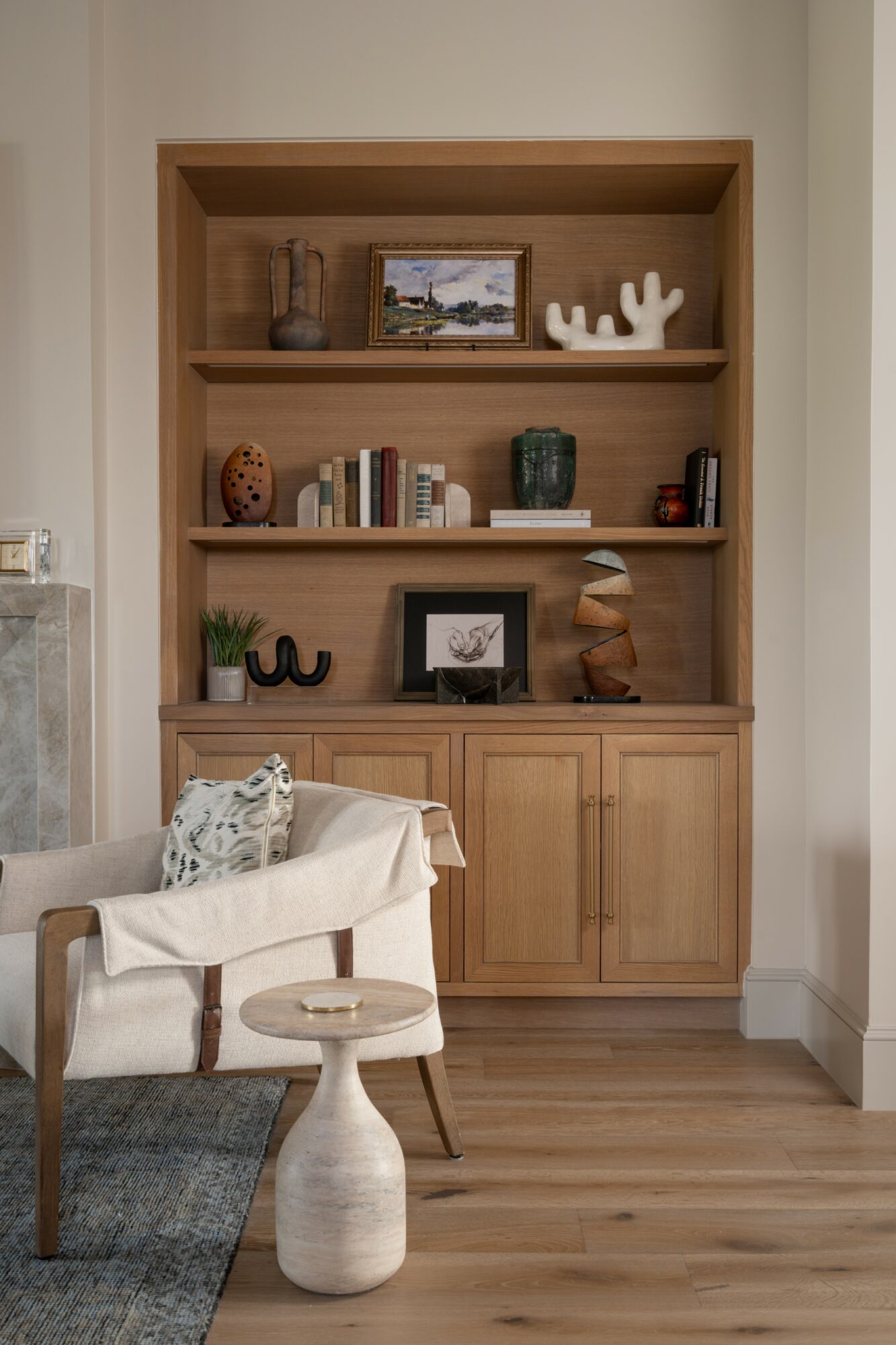 Wooden bookshelf with decorative items and books, part of a living room with a white armchair and a small table.
