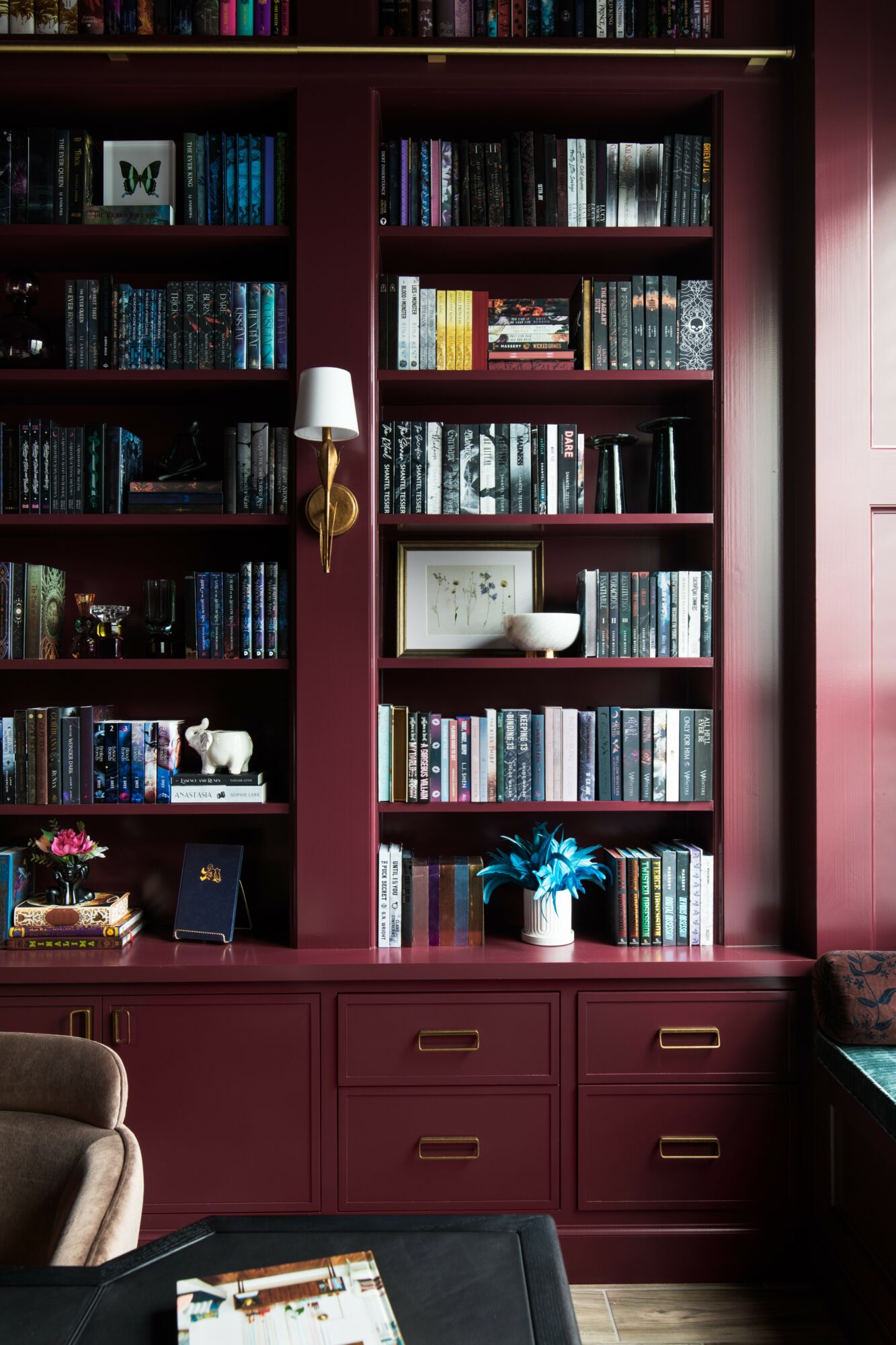 Bookshelves filled with books, a white lamp, a potted plant, and decorative items in a room with maroon walls.