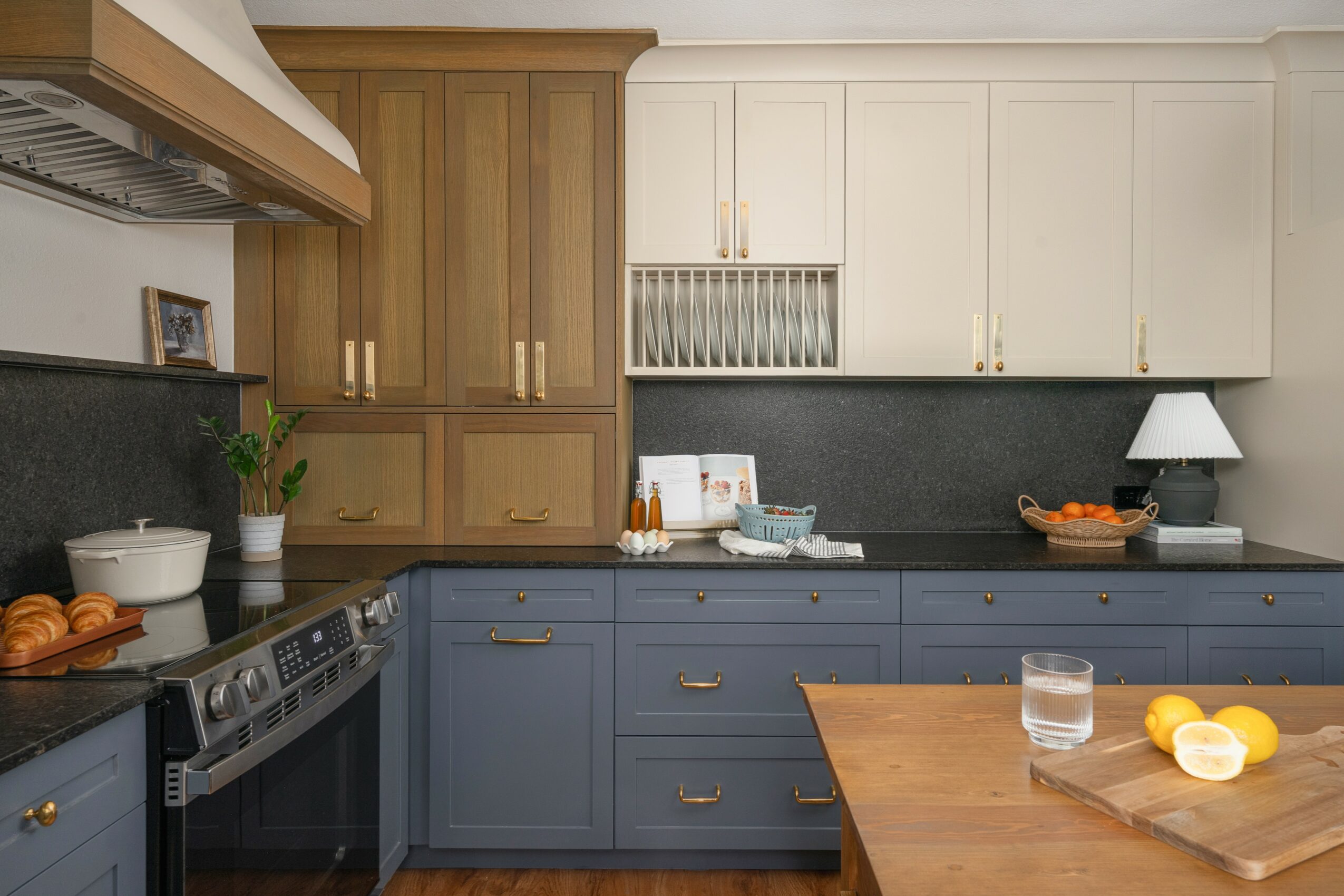 Kitchen with wooden and white cabinets, black countertop, blue lower cabinets, and a wooden table with lemons and a glass of water.