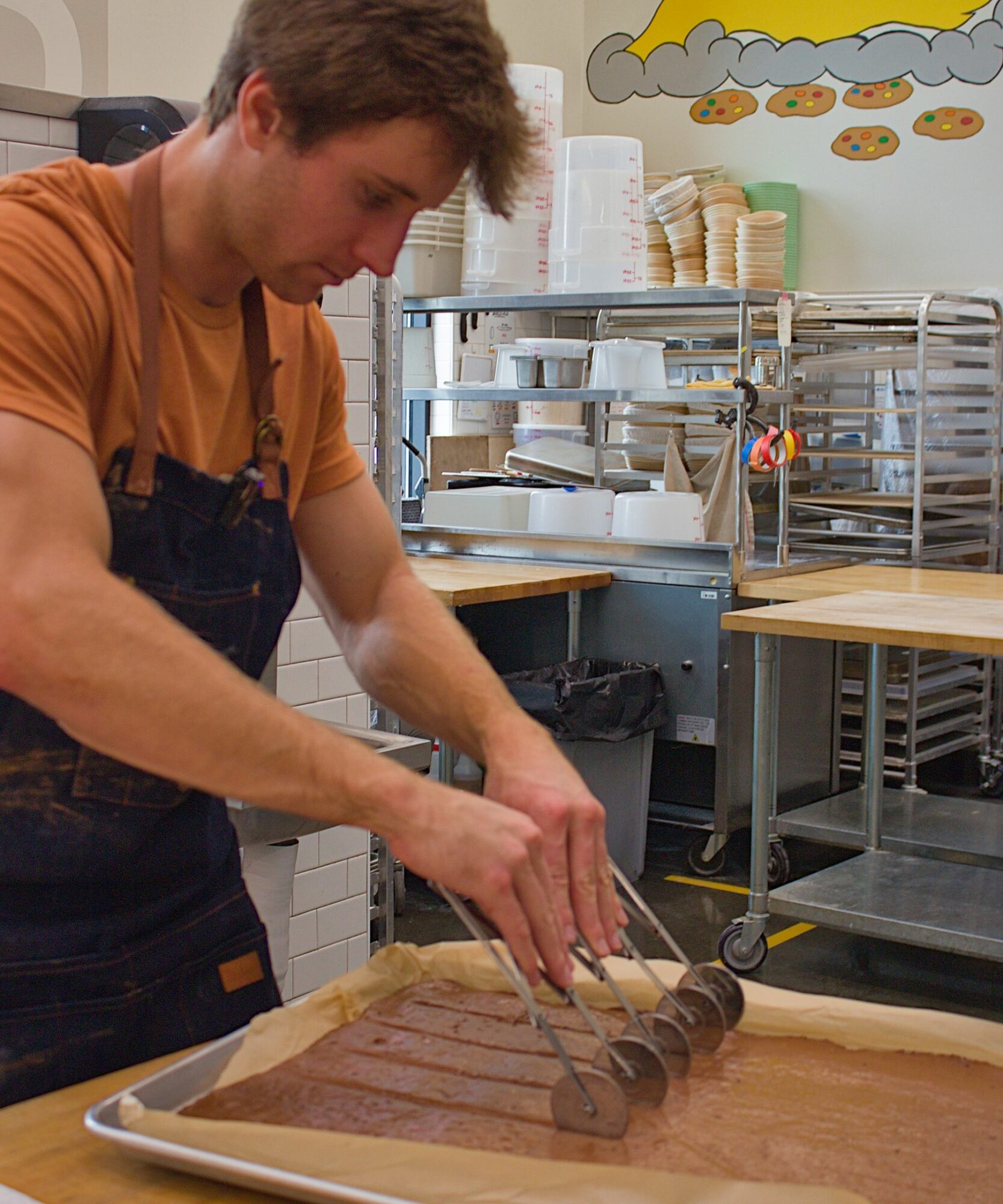 Person slicing rolled chocolate cake on a tray in a kitchen or bakery setting.