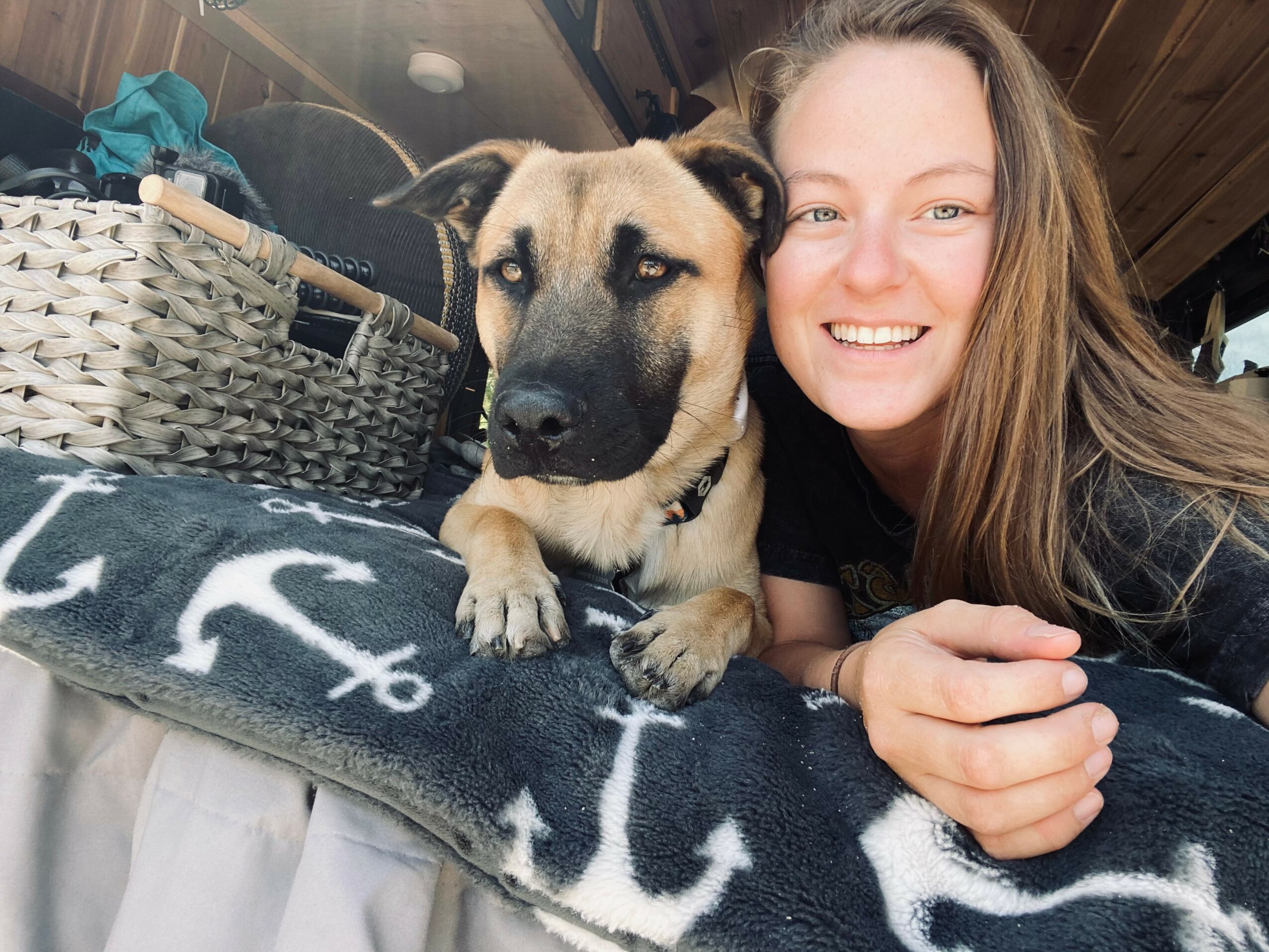 Woman and dog lying on blanket with anchor pattern, smiling at camera.