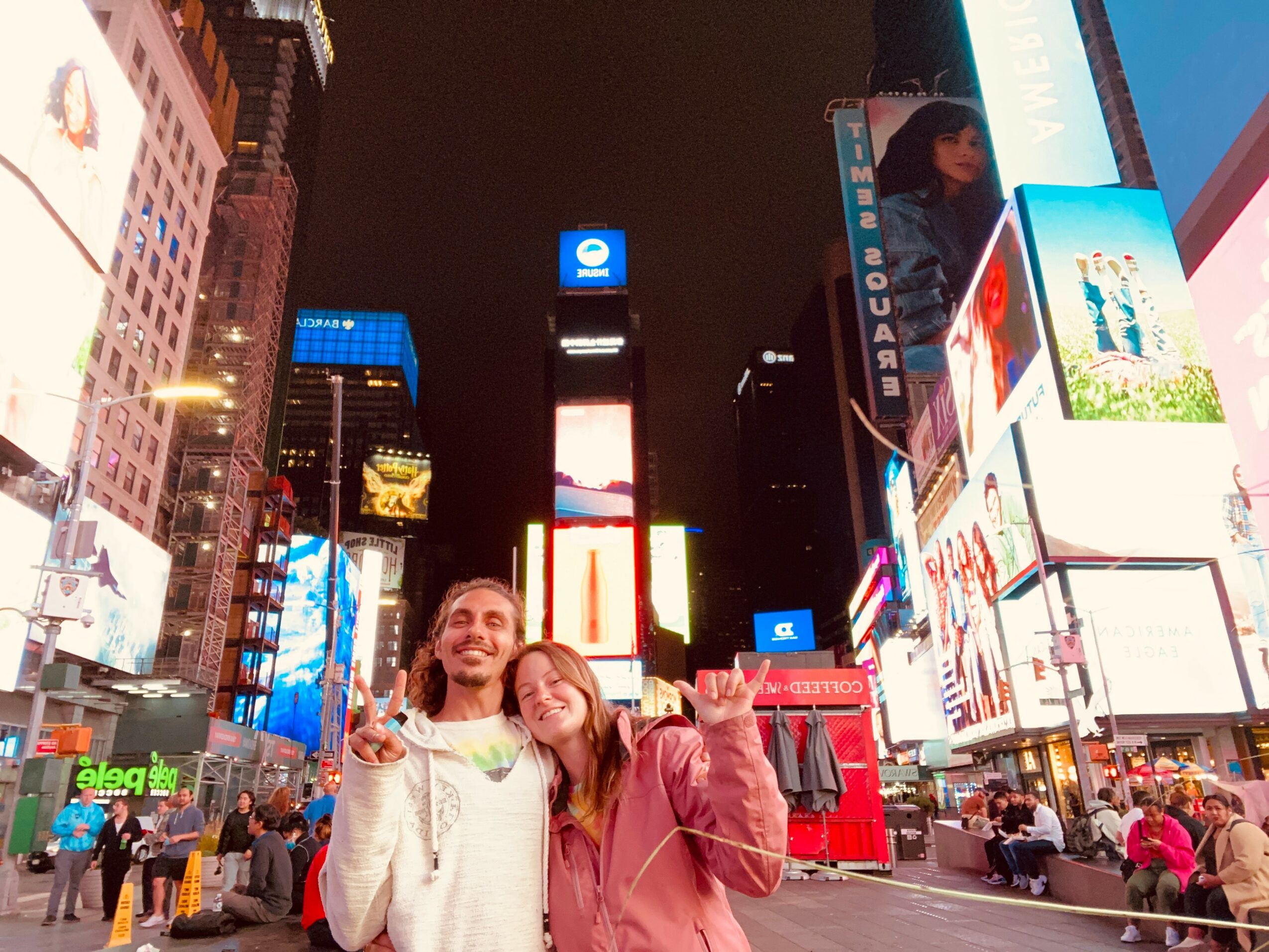 People standing in Times Square at night with bright digital billboards and buildings in the background.