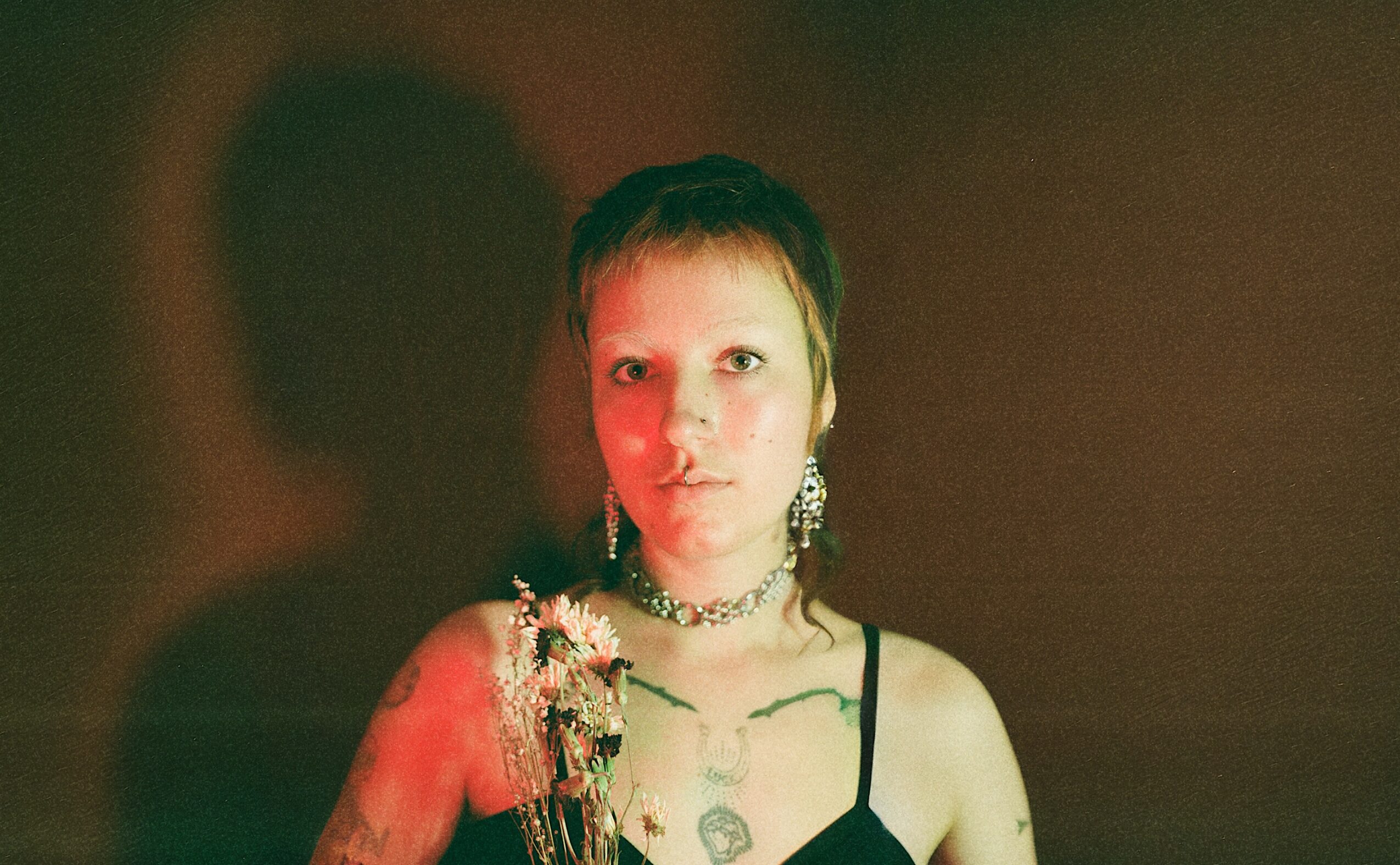 Person with short hair and earrings, wearing a black top, standing against a dark background.