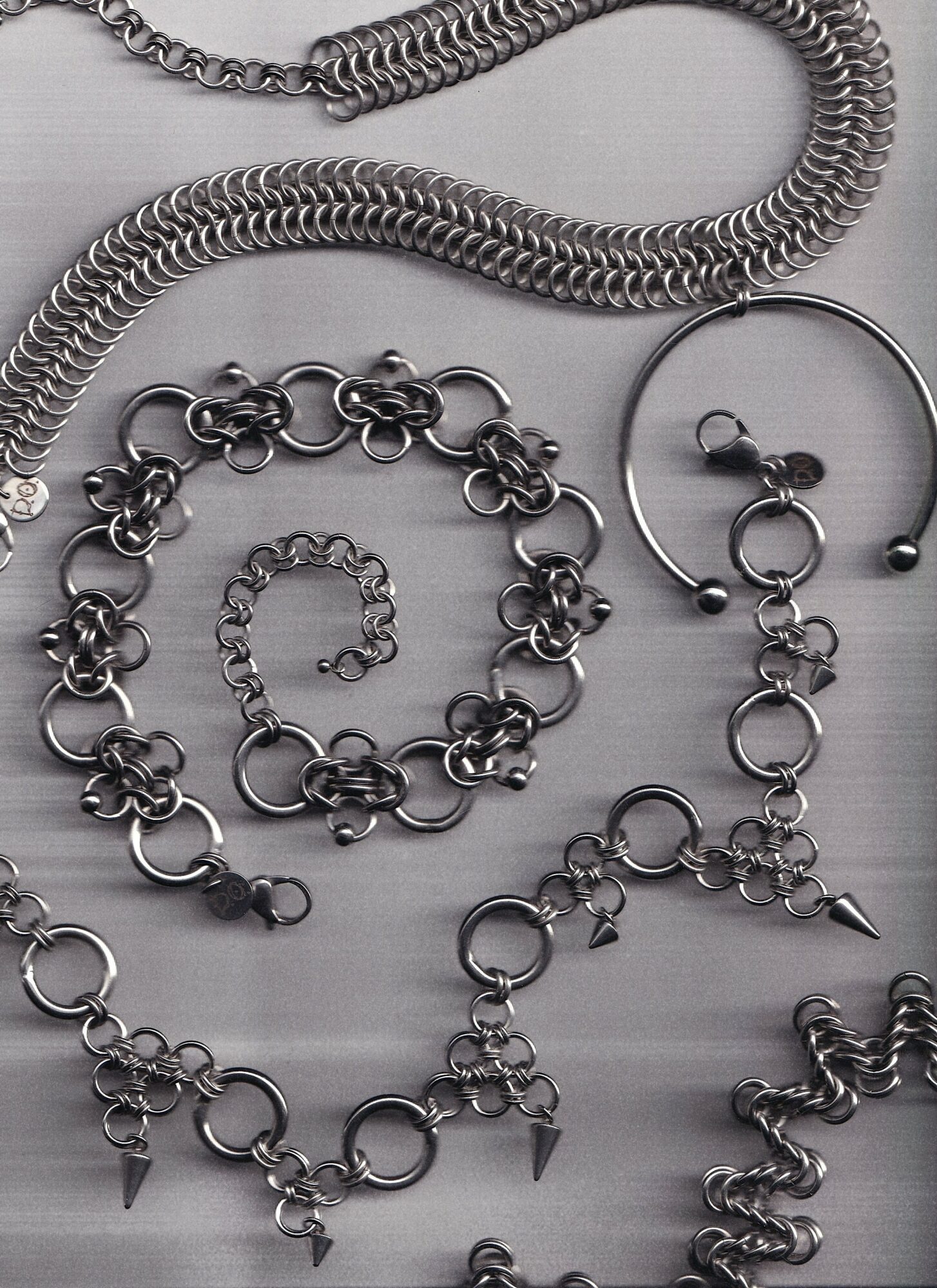 Collection of silver jewelry including a chain, bracelet, bangle, and rings with various links and charms.
