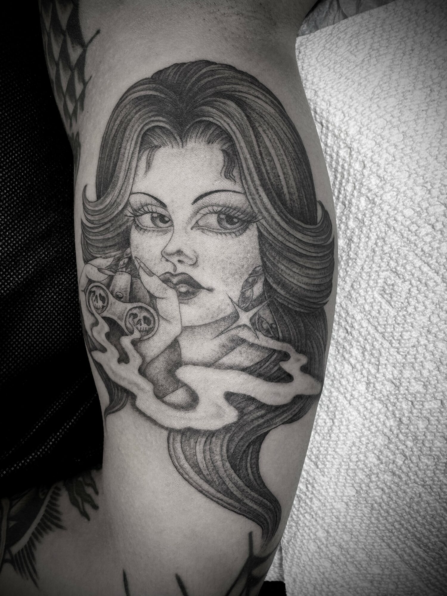 Black and gray tattoo of a woman's face with flowing hair and smoke around her neck.