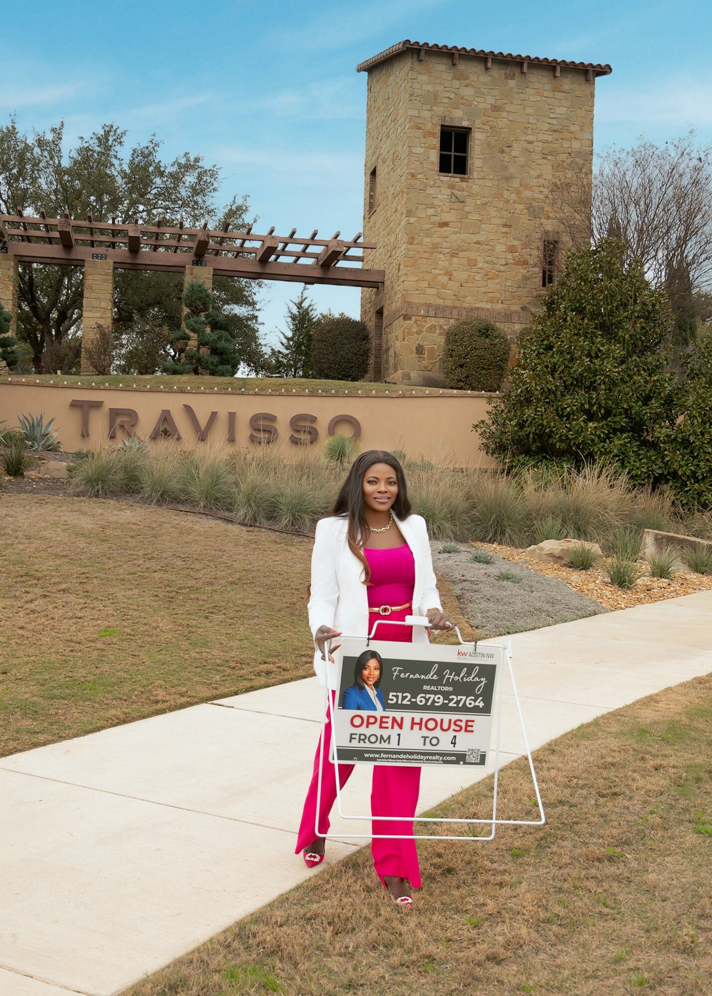 Woman holding a sign advertising an open house event, standing on a sidewalk with a stone tower and greenery in the background.