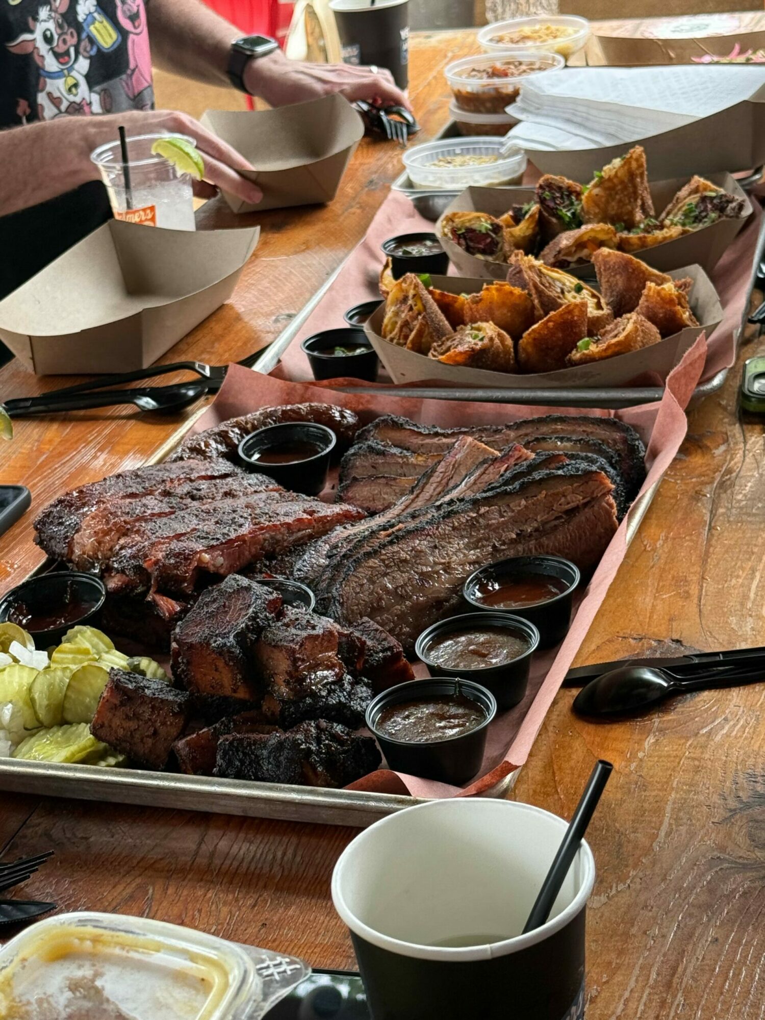 Table with fried food, dipping sauces, and a cutting board with meat and lemon slices, viewed from above.