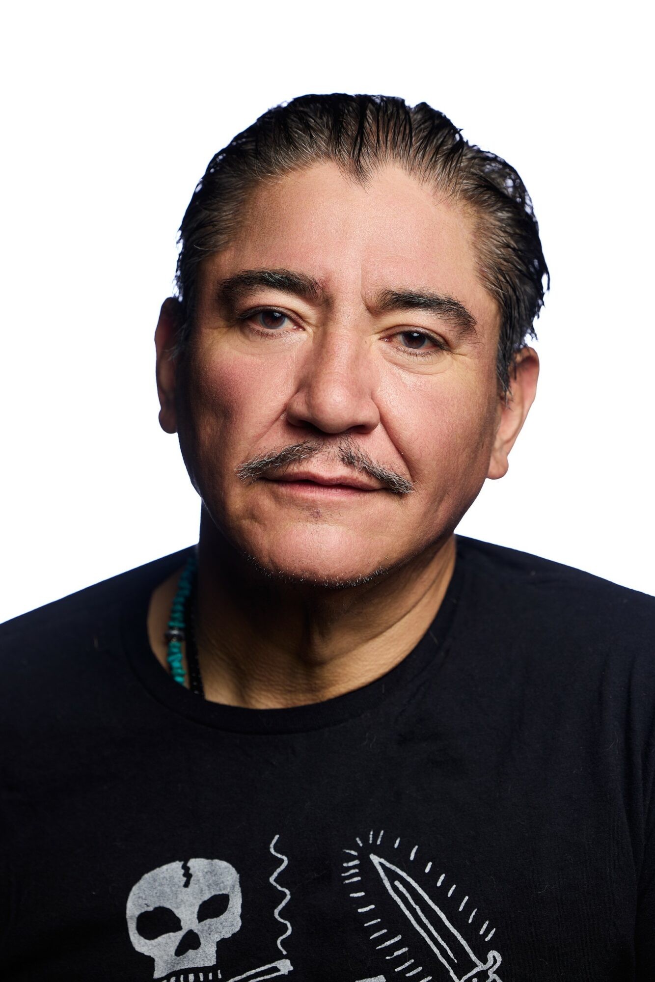 Portrait of a middle-aged man with dark hair, mustache, and goatee, wearing a black shirt with white graphic, against a white background.