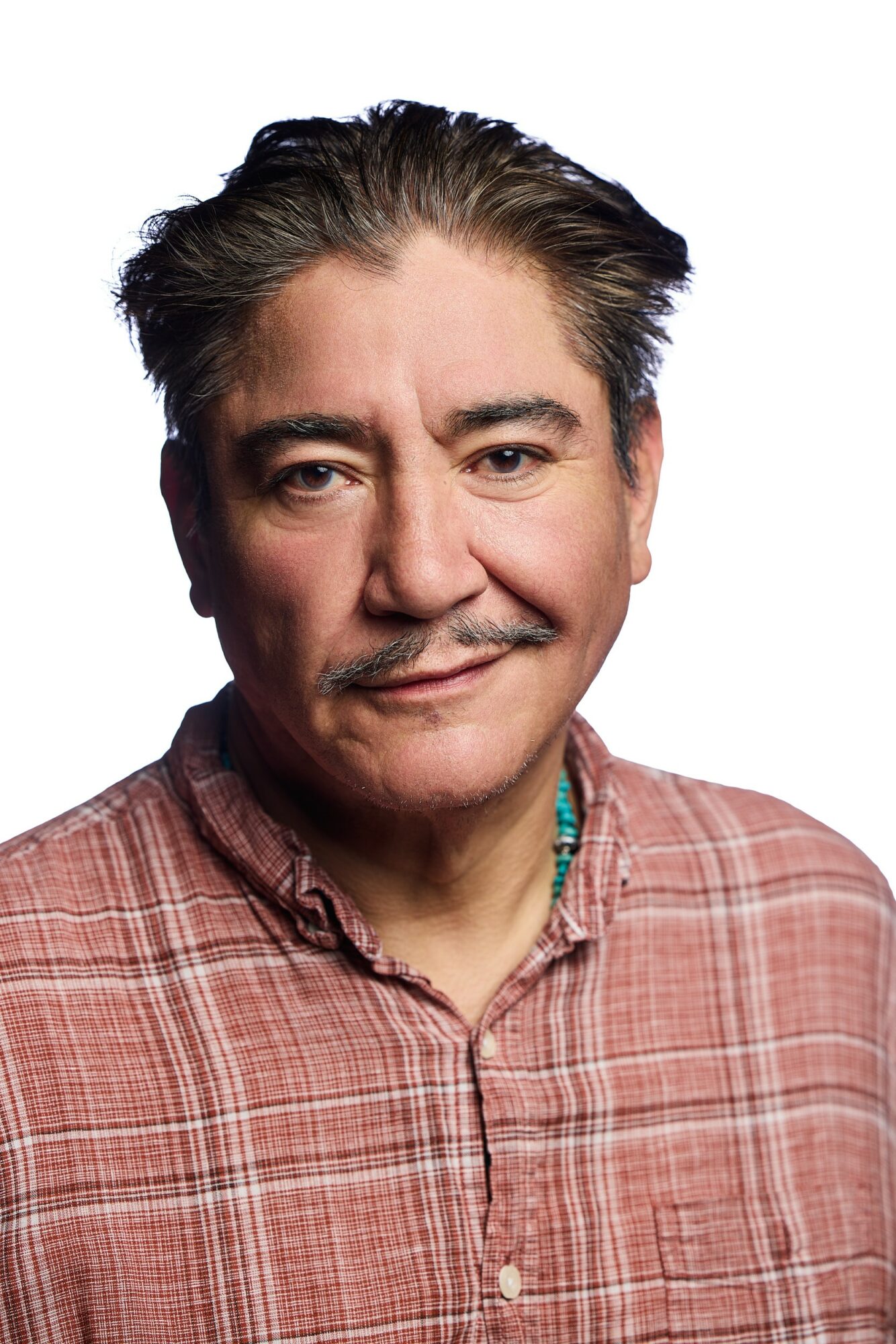 Portrait of a middle-aged man with dark hair, mustache, wearing a plaid shirt, smiling slightly.