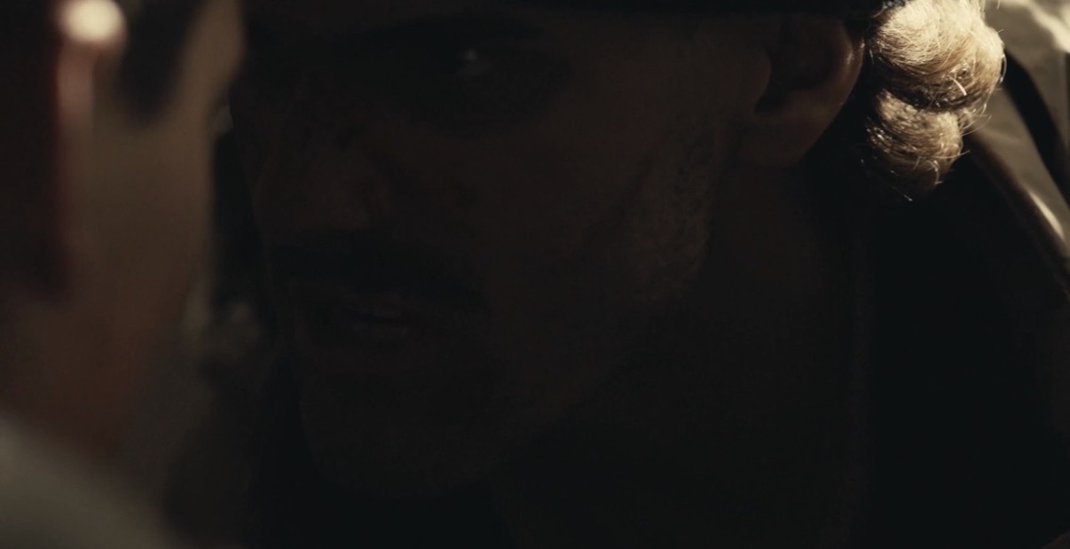 Darkly lit close-up of a person's face with visible hair and partial facial features.