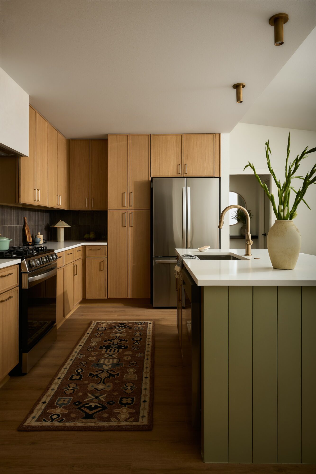 Kitchen with wooden cabinets, stainless steel refrigerator, and a green island with a plant in a vase.