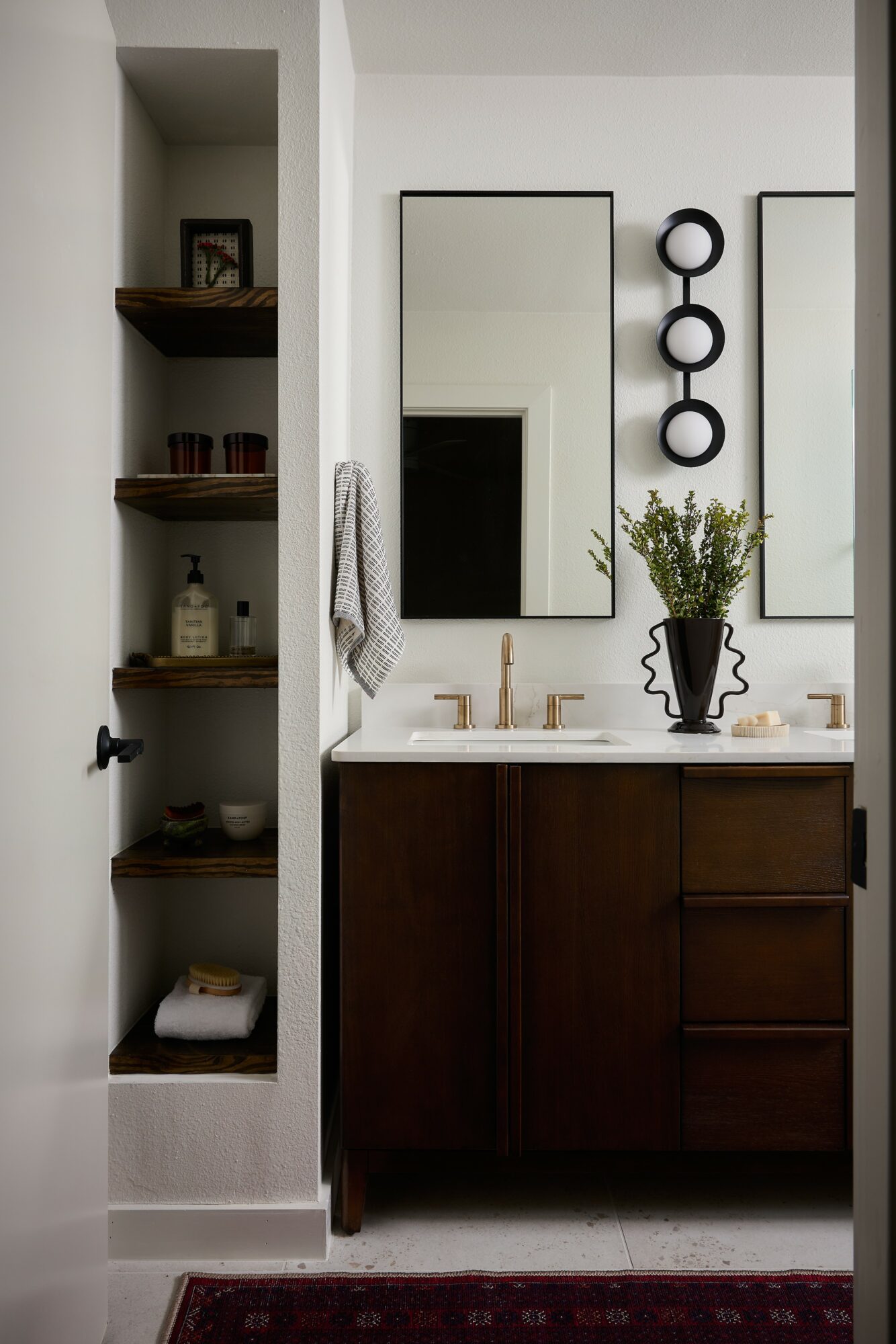 Bathroom vanity with mirror, shelves on the left, and decorative wall art, with a plant on the countertop.