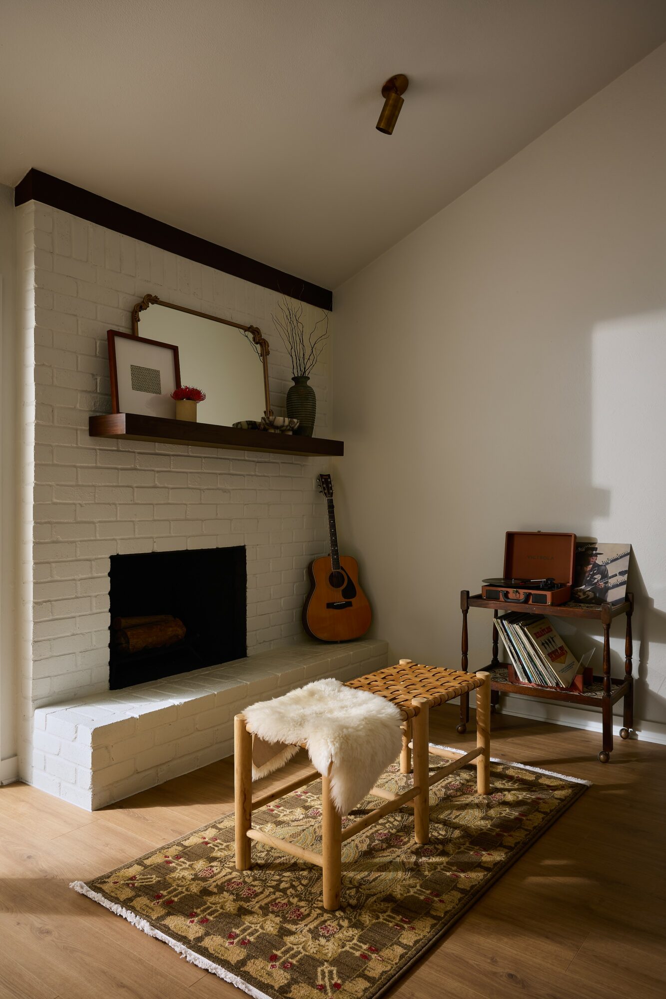 Living room corner with a white brick fireplace, guitar, shelf with decor, small table, and a rug.