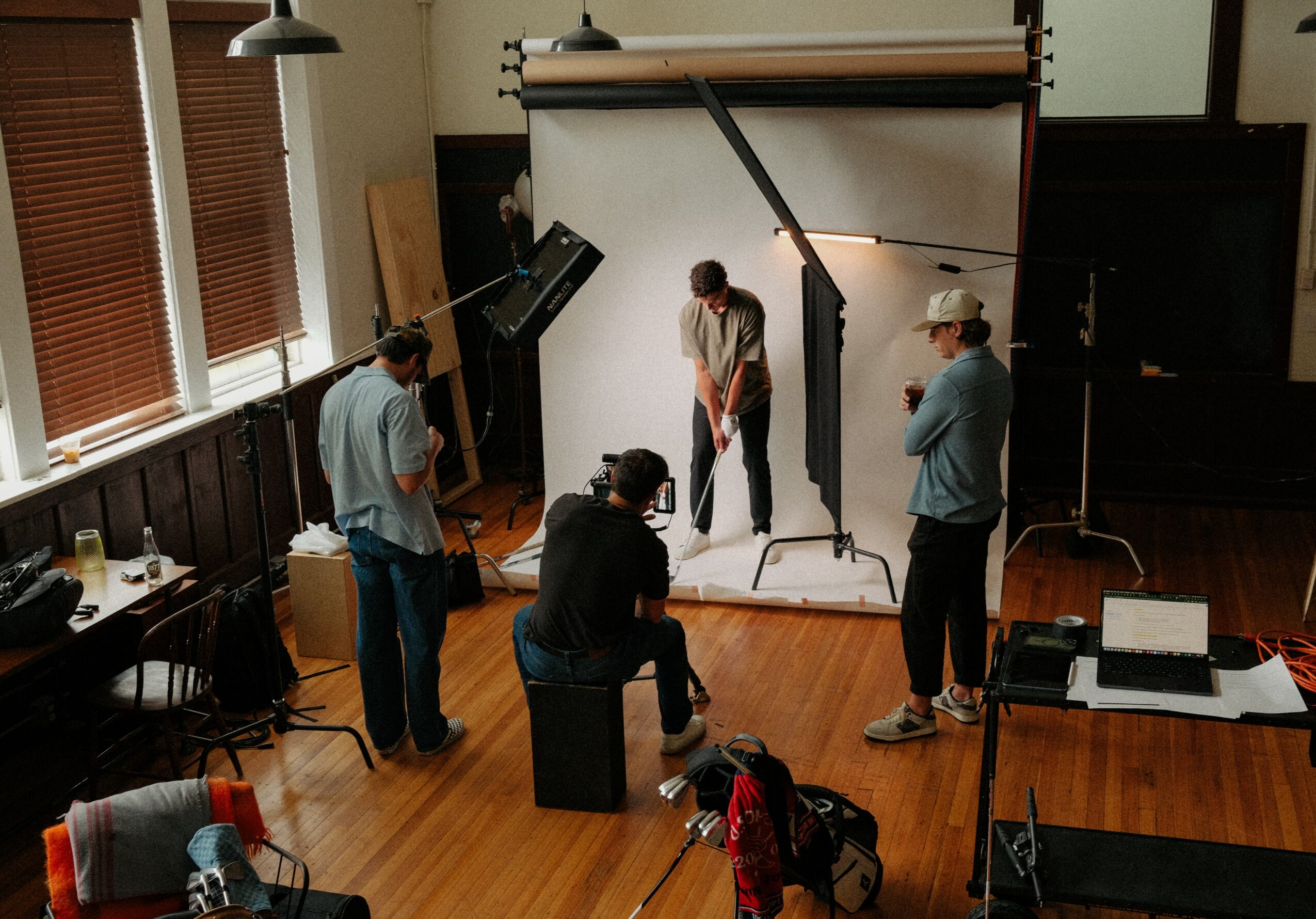 People in a photography studio setting up a photo shoot with a white backdrop and lighting equipment.