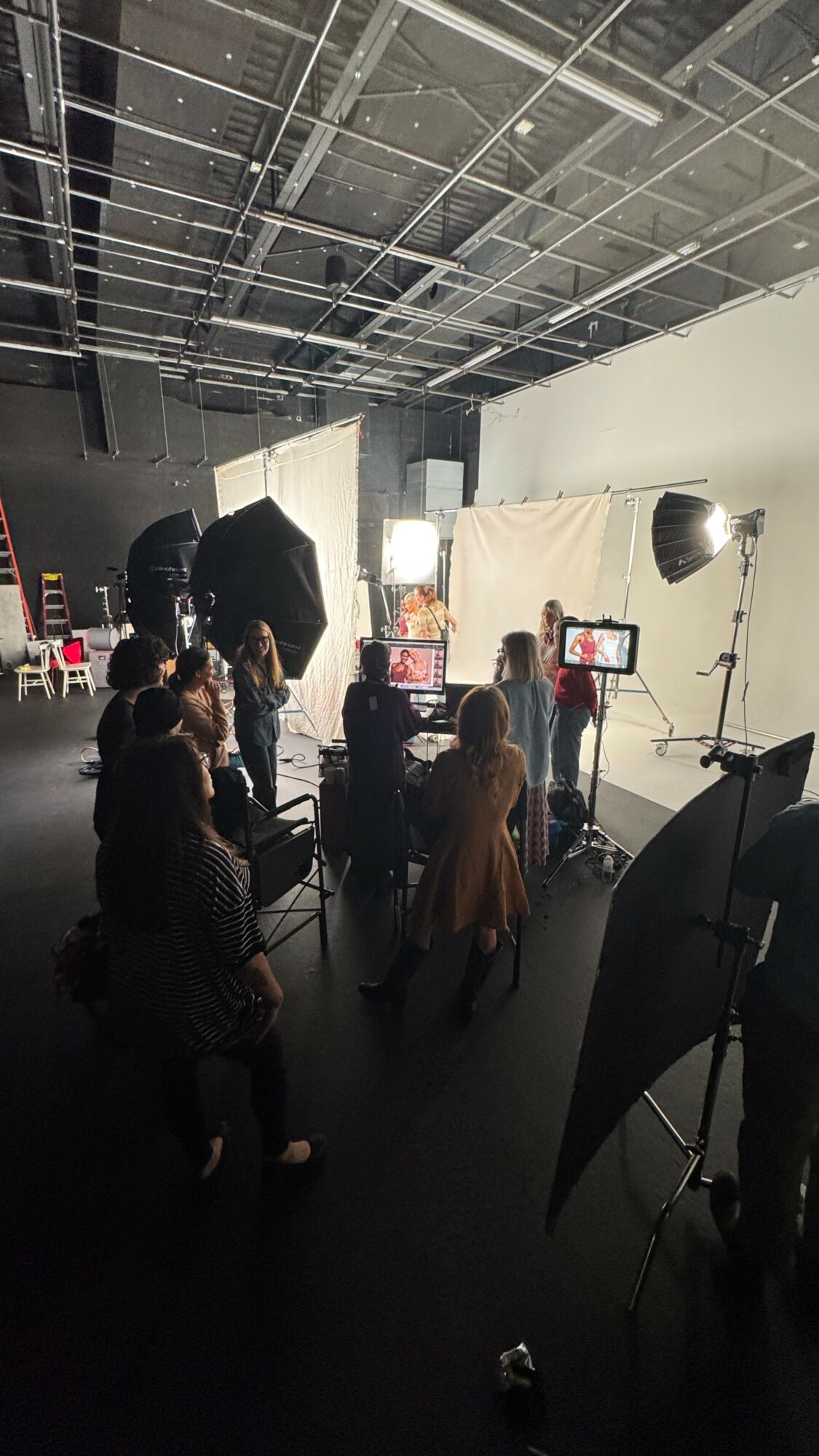 People in a studio setting with lighting equipment and a white backdrop, preparing for a photo or video shoot.