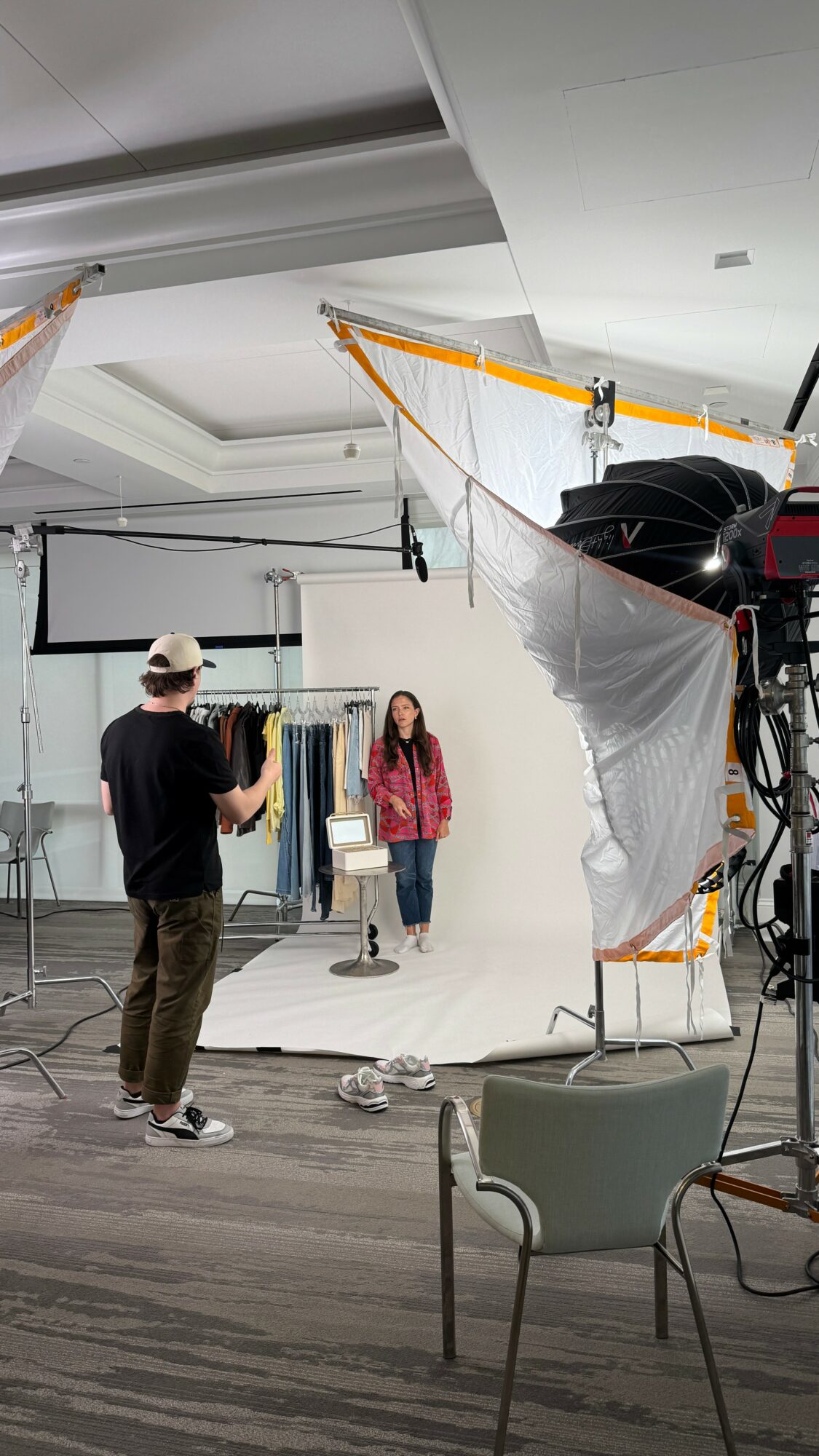 People in a photography studio with lighting equipment and a white backdrop, one person taking a photo of a woman.