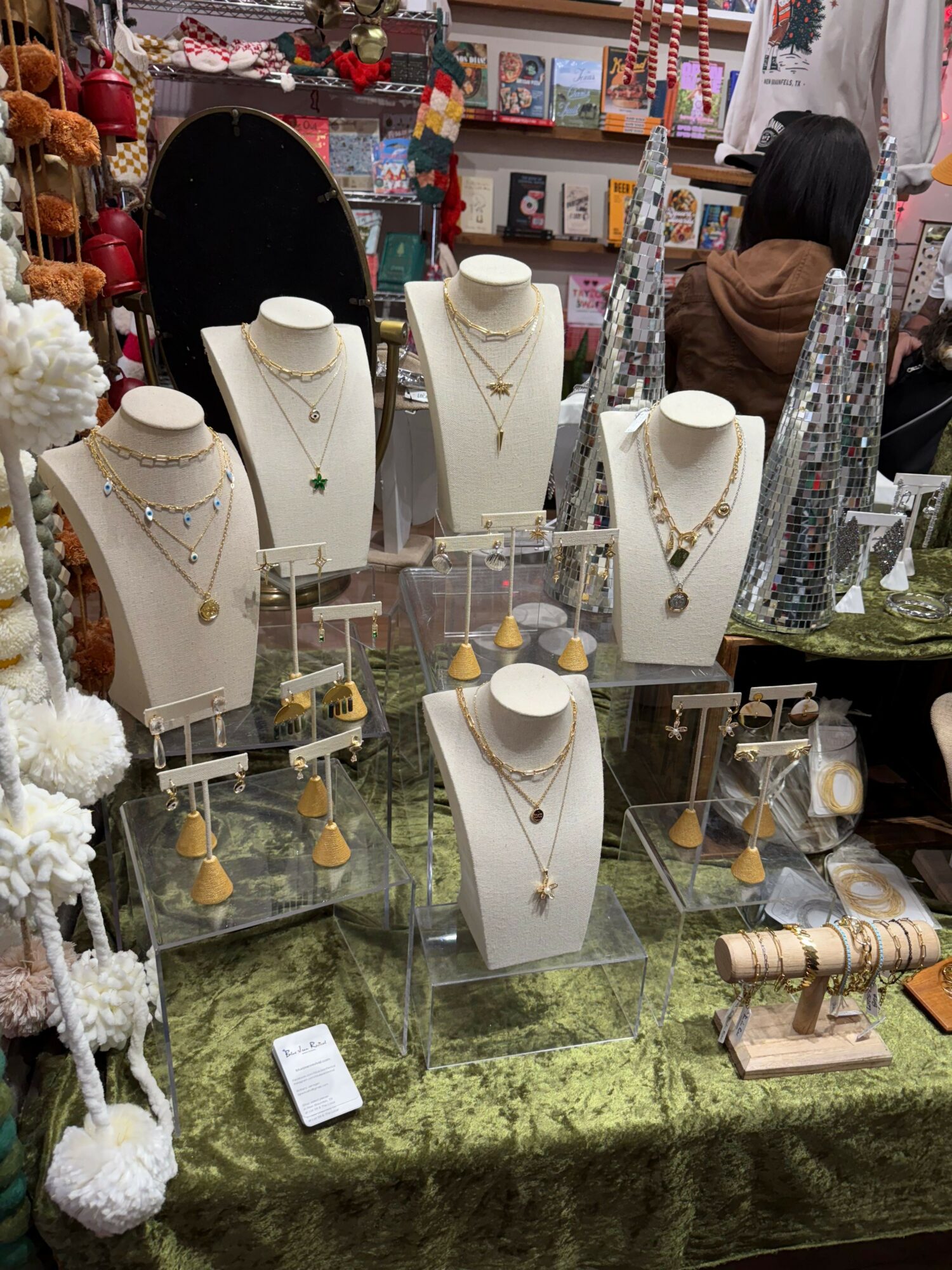 Display of white jewelry busts with necklaces, on a glass table with a green textured surface, in a busy market setting.