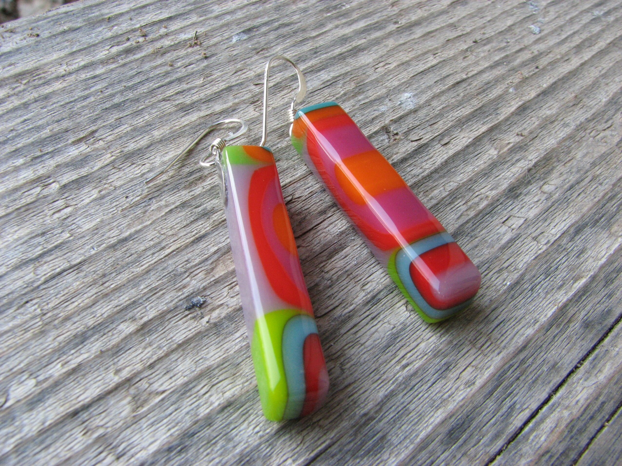 Colorful glass earrings with red, orange, green, and gray patterns on a wooden surface.