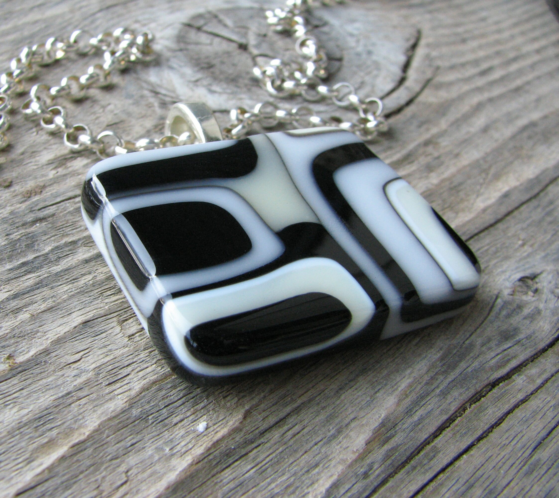 Black and white patterned glass pendant necklace on wooden surface.