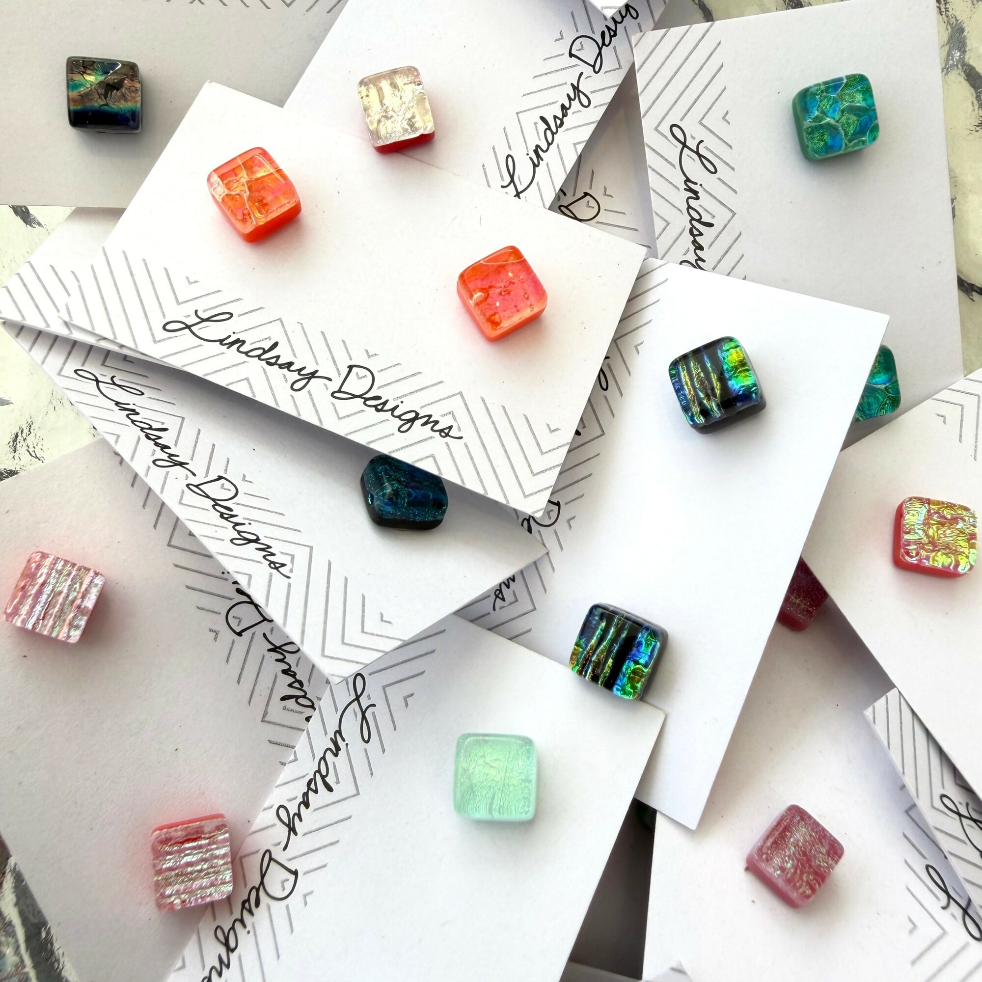 Colorful square beads on white cards with handwritten text, scattered randomly.