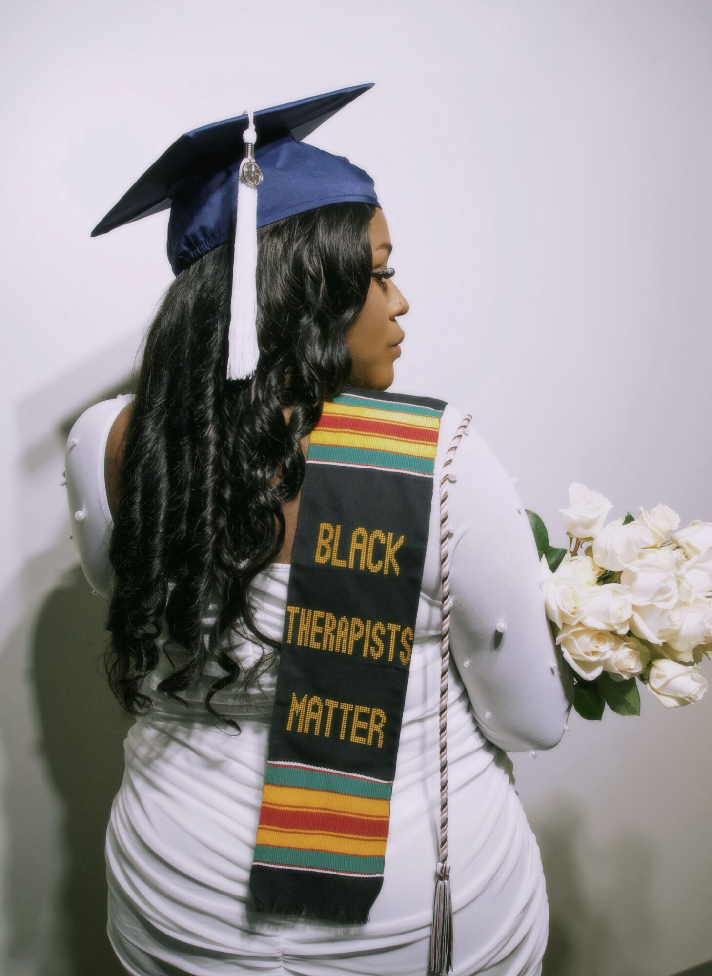Profile of a woman in graduation cap and gown holding a bouquet of white flowers.