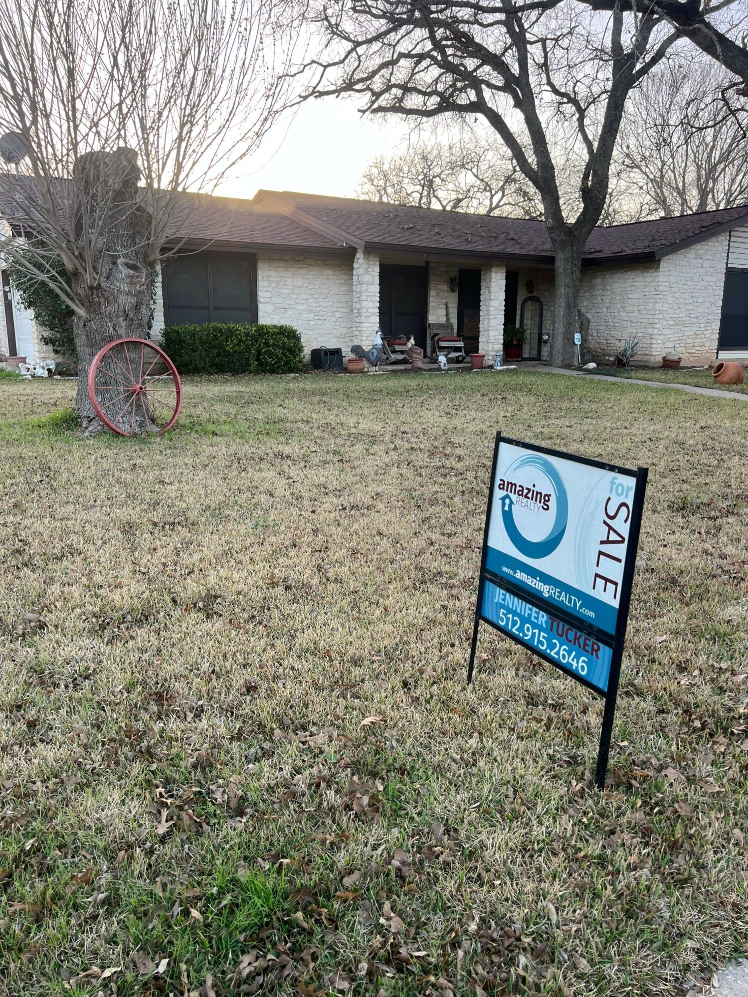 Sign on grass advertising a sale, with a house and trees in the background.
