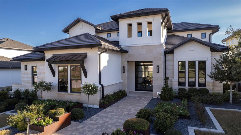 Modern house with white exterior, multiple windows, and a landscaped front yard with plants and a pathway.