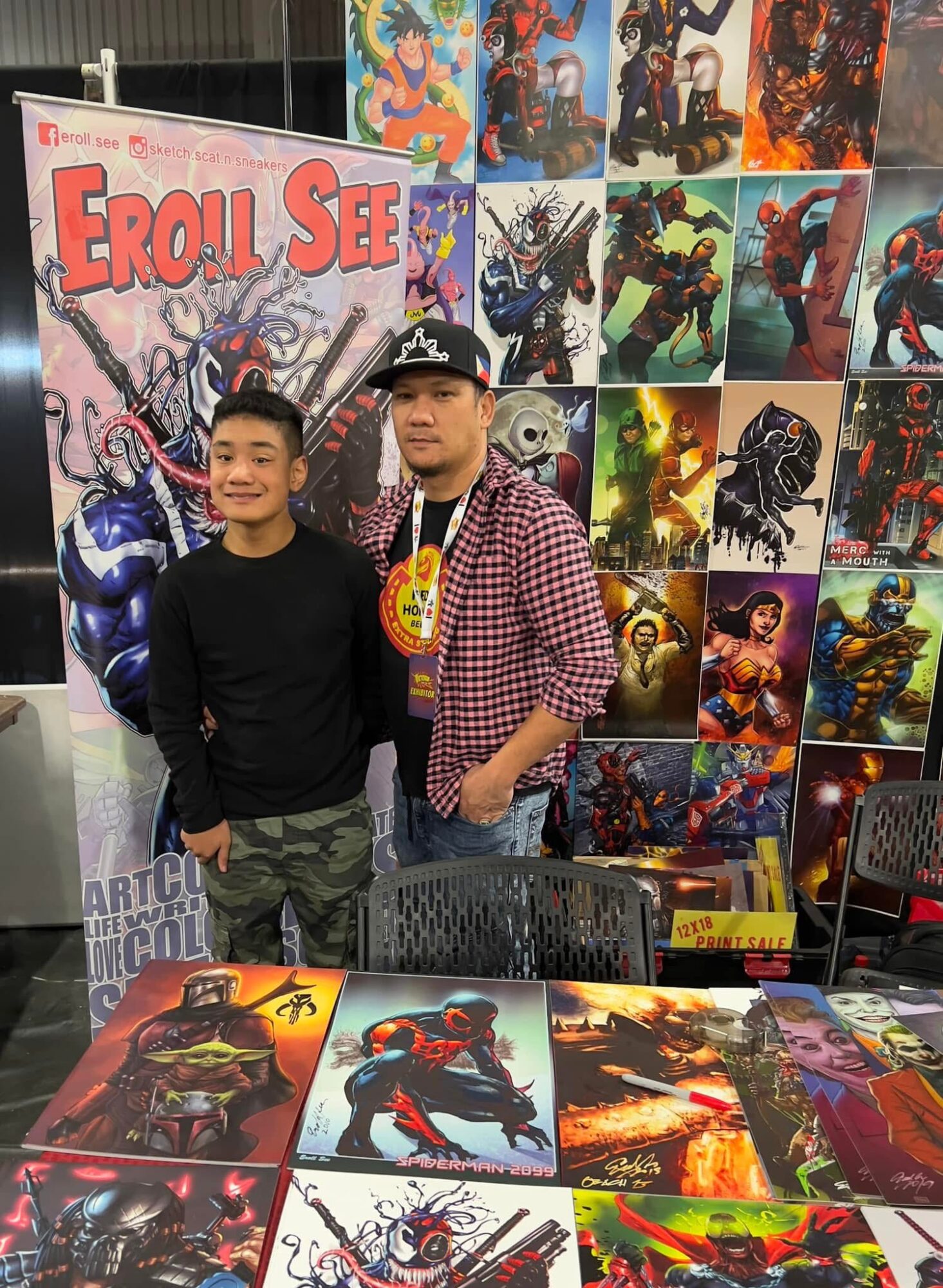 Two people standing in front of a comic book display, with artwork and posters behind them, smiling at the camera.