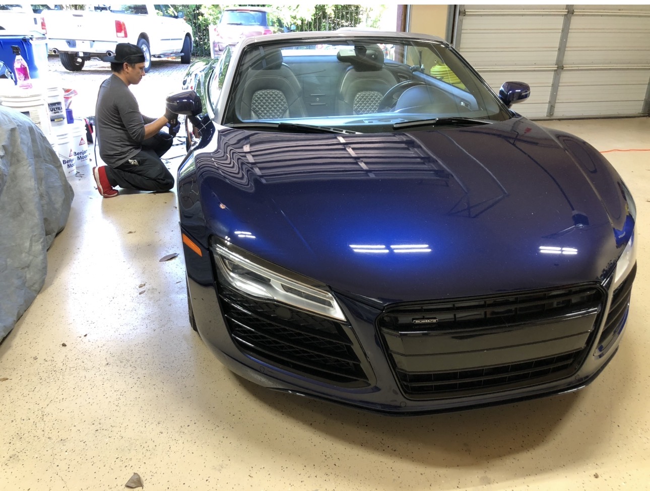 Dark blue convertible sports car parked indoors with a person working nearby, garage door in background.