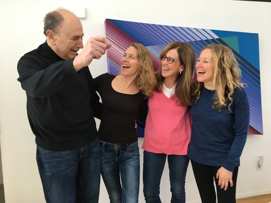 Four people smiling and laughing together, standing in front of a colorful geometric wall art.