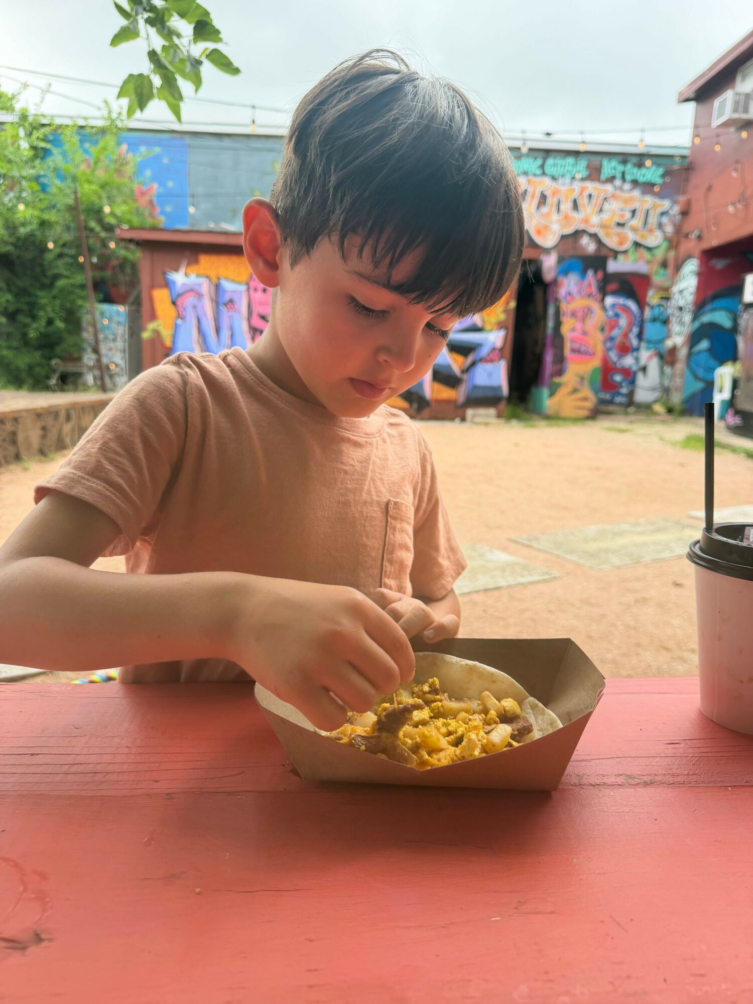 Child with dark hair and light-colored shirt eating popcorn at a table outdoors.