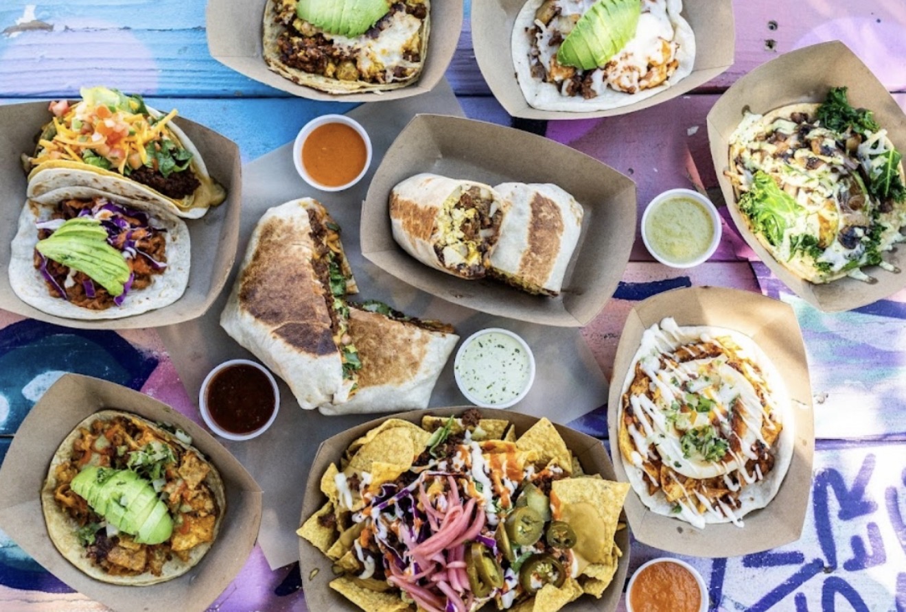 Assorted tacos and nachos with various toppings and sauces on colorful table, viewed from above.