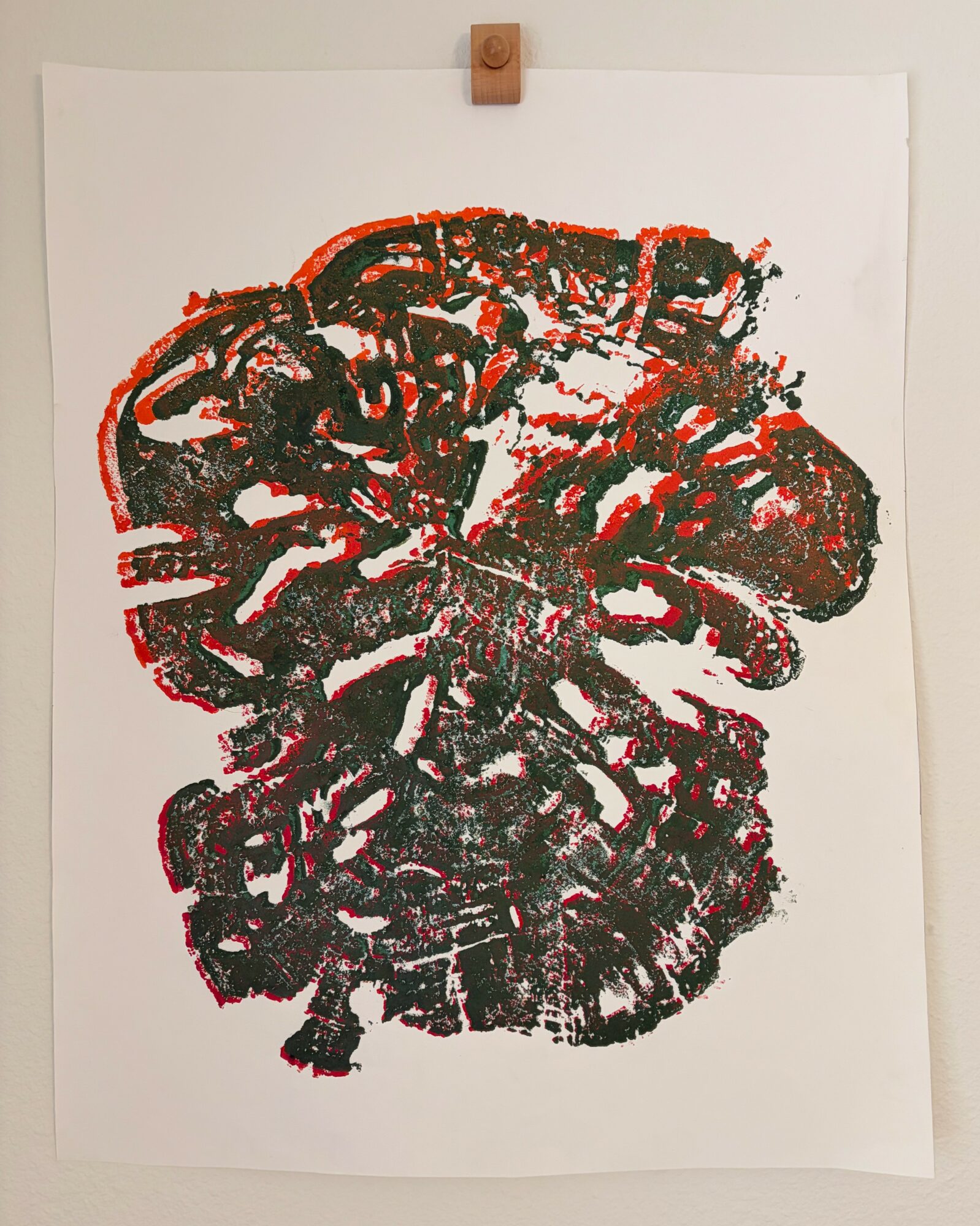 Abstract artwork with red and black colors on white background, resembling a face or mask, mounted on a wall with a clip.