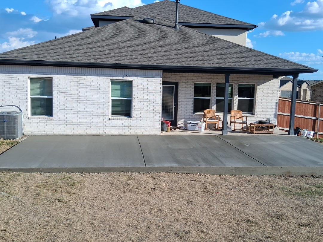 Backyard patio with seating area, concrete floor, house with brick exterior, and a wooden fence on the right.