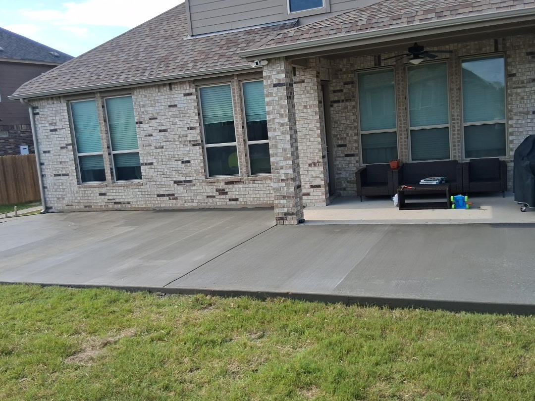 Backyard patio with outdoor furniture, concrete floor, brick house wall, and grassy lawn in front.