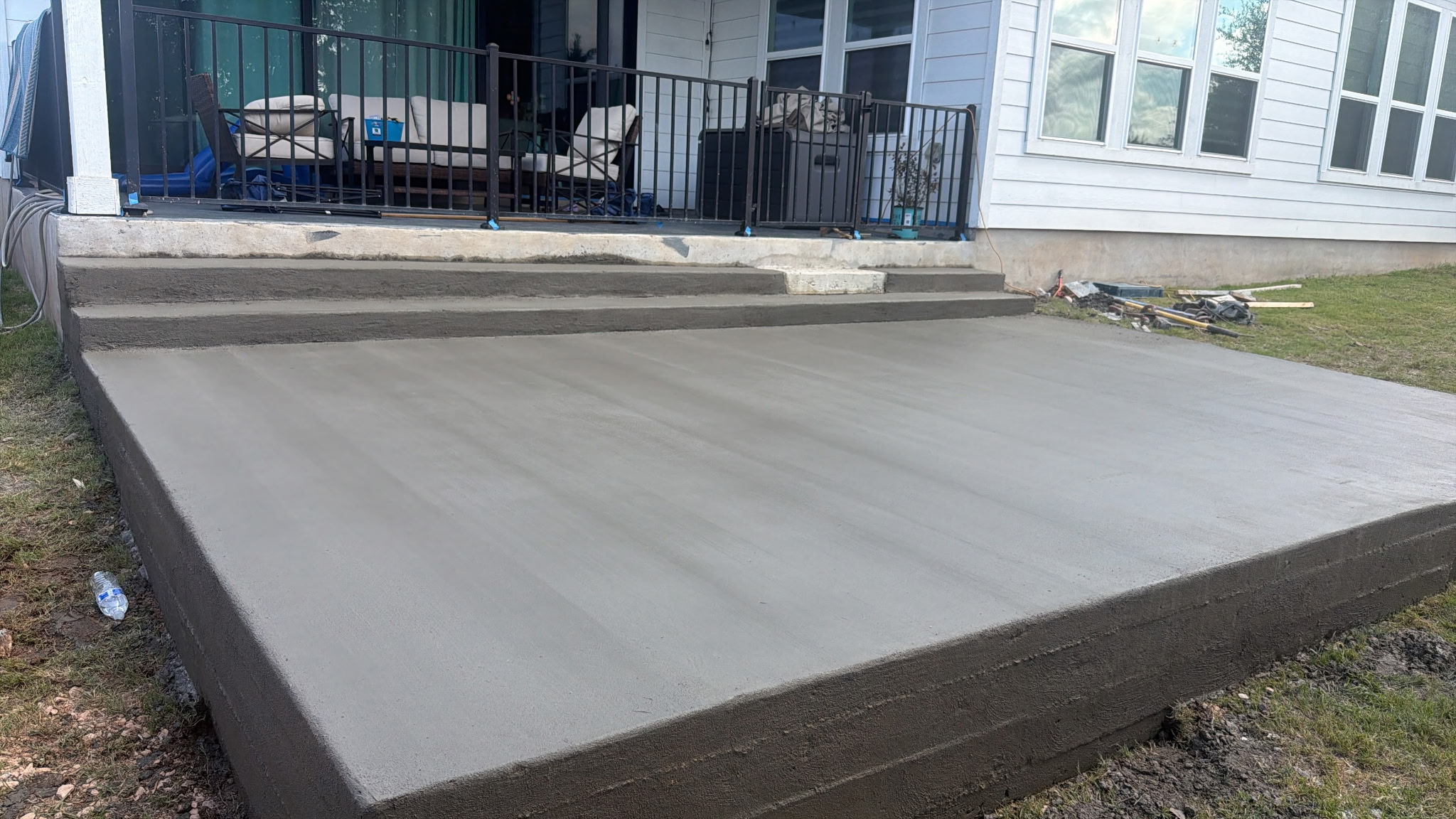 Freshly poured concrete slab in front of a house with a porch and outdoor furniture