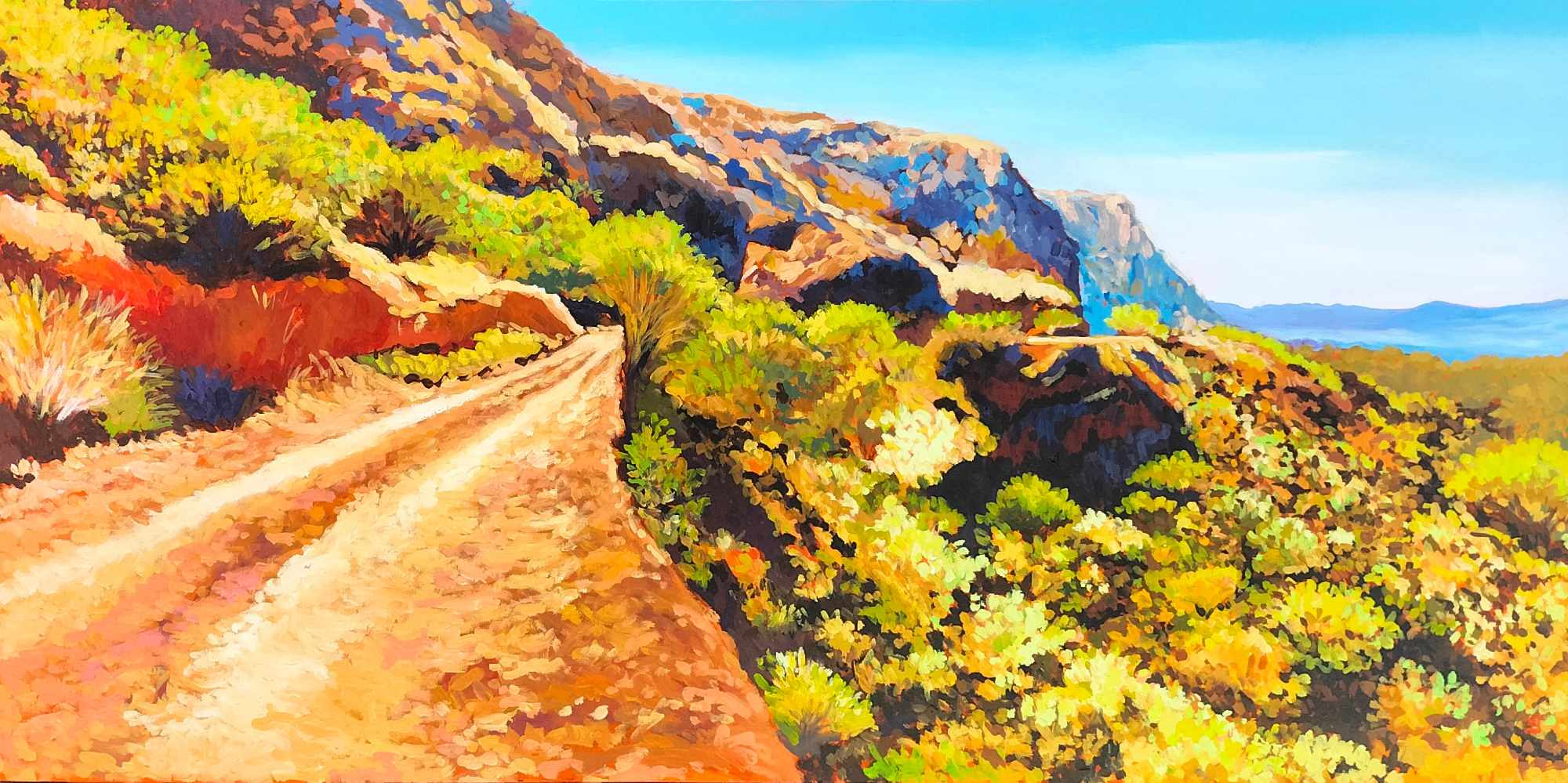 A dirt road winds through a colorful landscape with trees and mountains in the background.