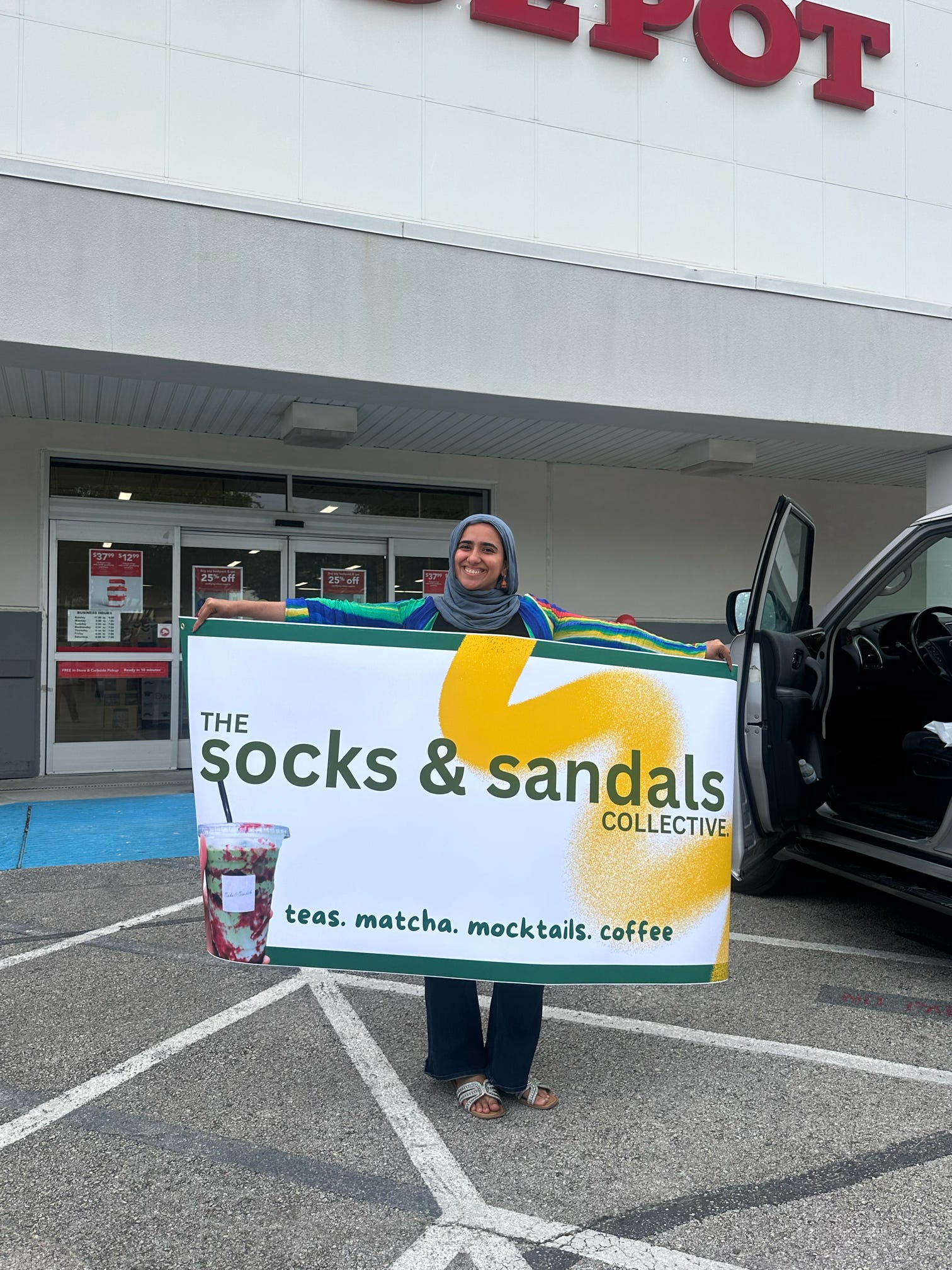 Person holding a large sign outside a store, smiling, with a shopping cart nearby.