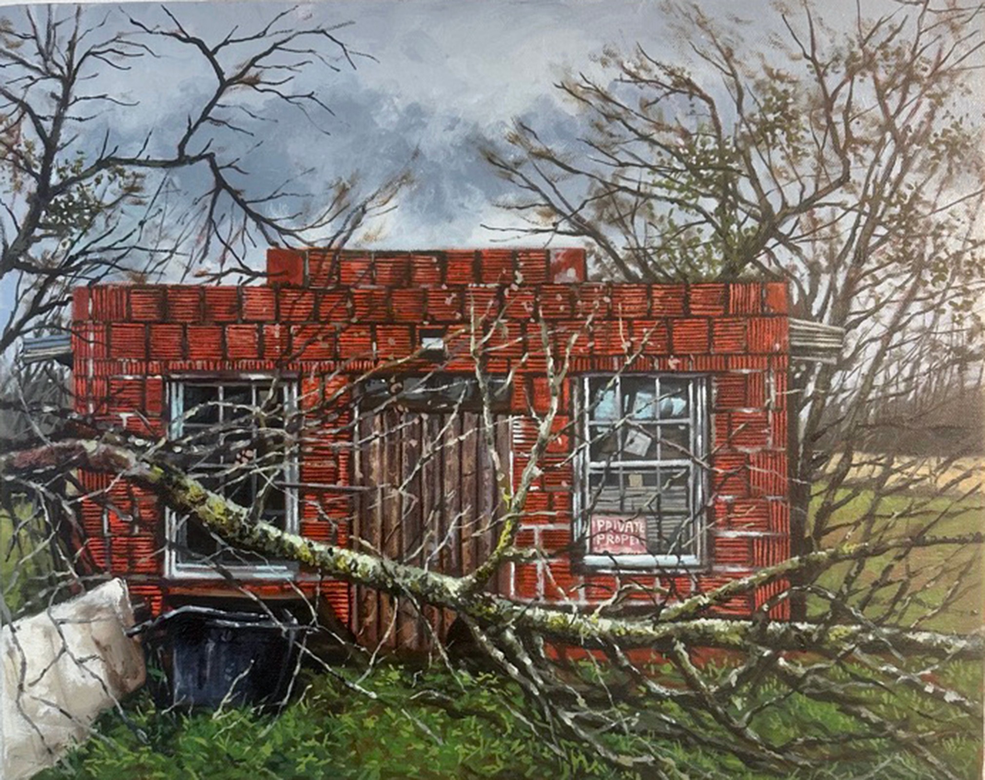 A small brick building with two windows, surrounded by trees and a fallen branch in front.