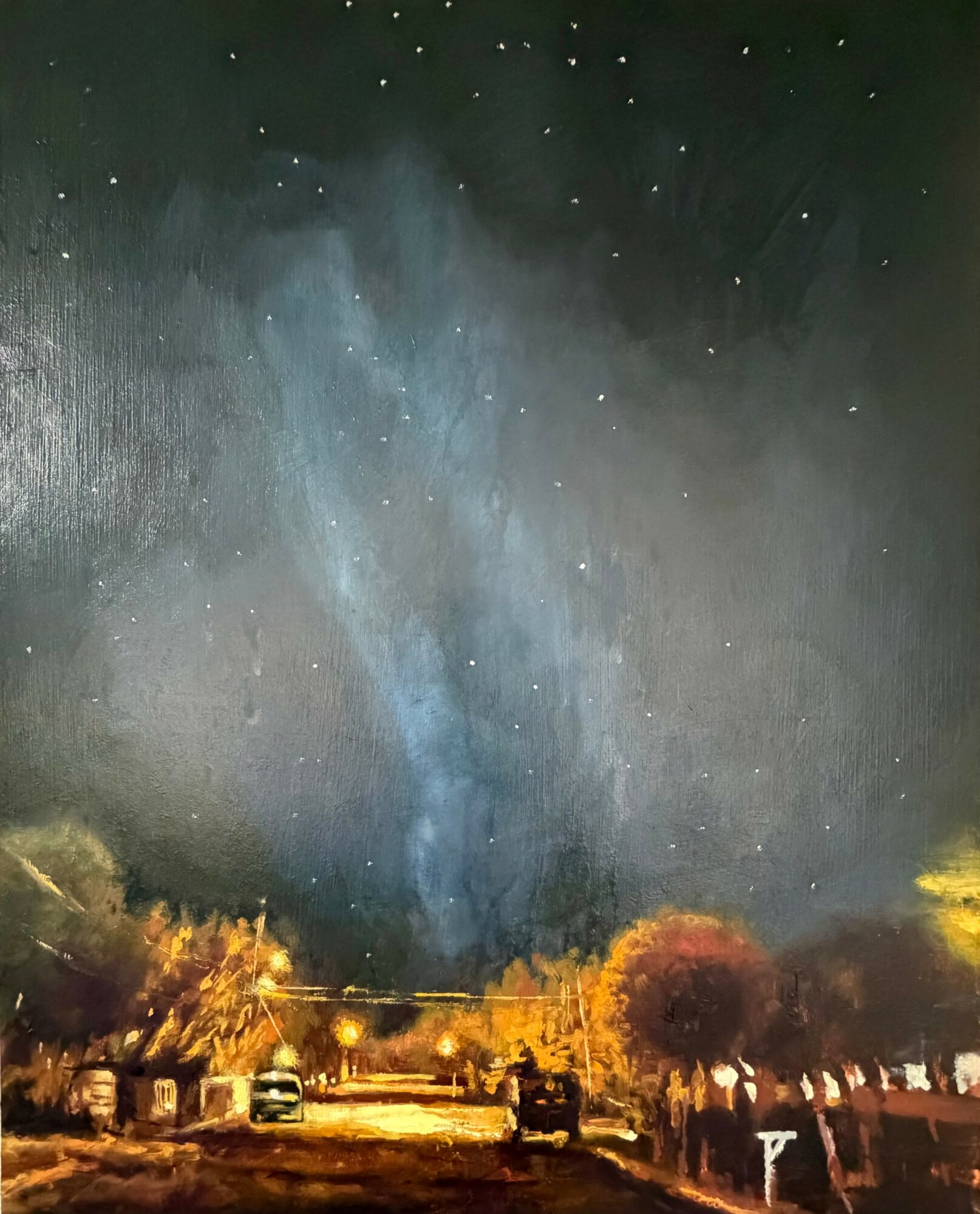Night sky with stars above a landscape with trees and vehicles, illuminated by streetlights.