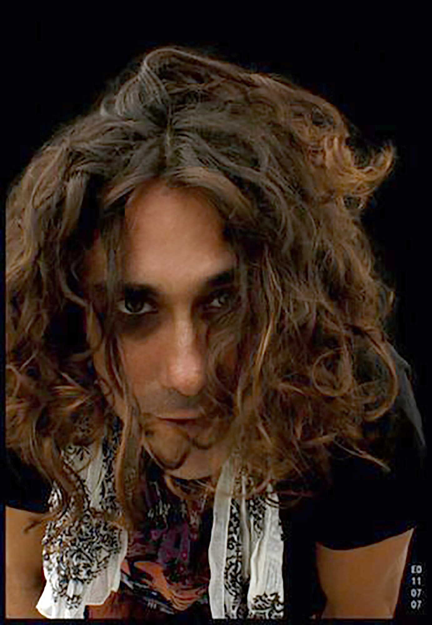 Woman with curly hair looking at camera, dark background, wearing a black top and patterned scarf.