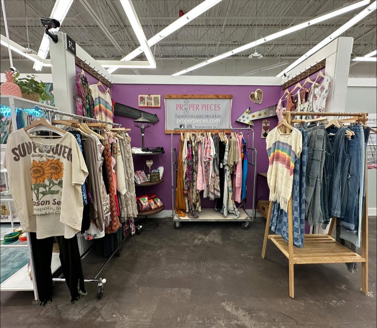 Clothing display with racks of colorful garments and a purple wall background, inside a store or market setting.