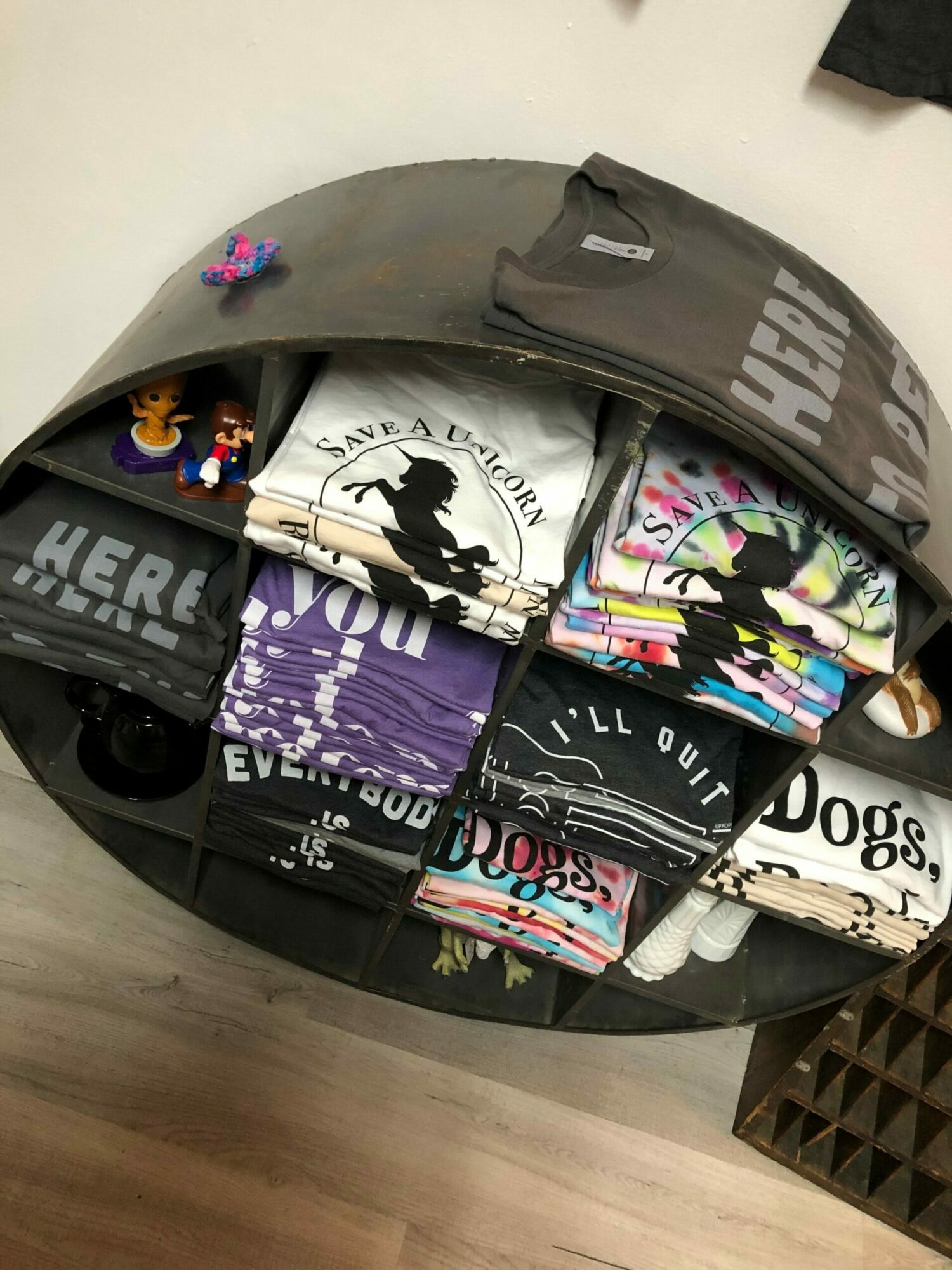 Open circular container with folded clothing, socks, and small toys inside, on a wooden floor.