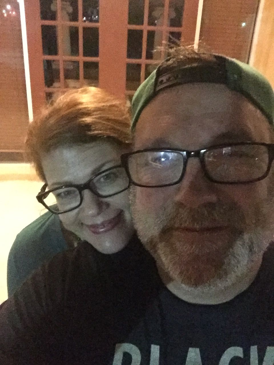 Two people wearing glasses, smiling, close together outdoors at night, with a building in the background.