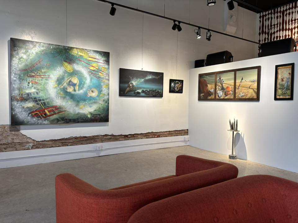 Art gallery with paintings on white walls, red sofa in foreground, and track lighting overhead.