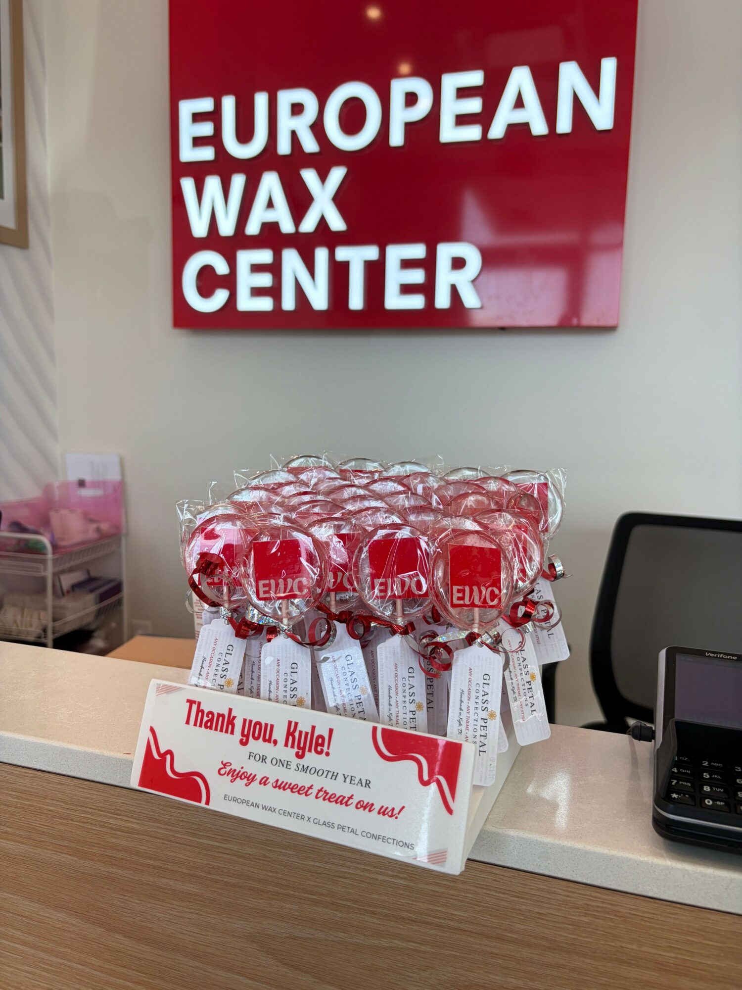 Counter with wrapped candies and a thank you note, behind a sign for European Wax Center, on a wooden surface.