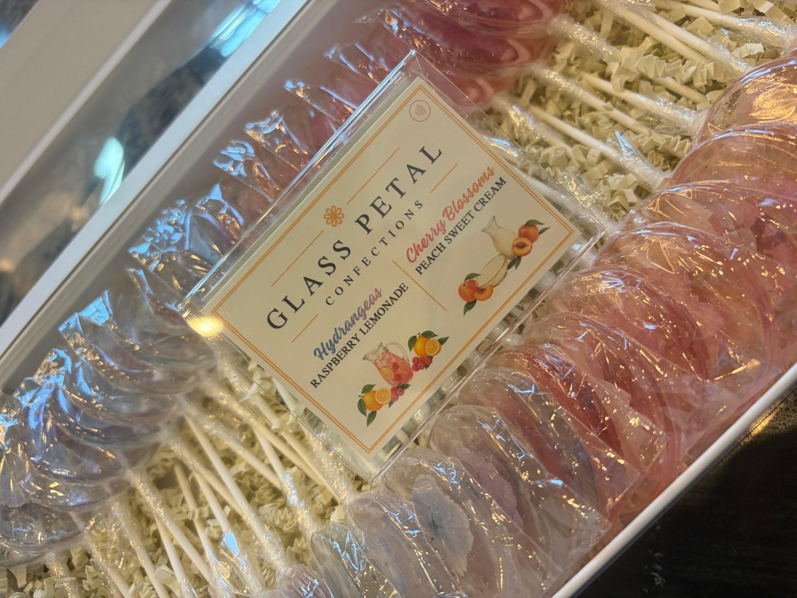 Display of glass petal candies with a sign reading 'Glass Petal' and colorful floral illustrations, arranged in a tray.