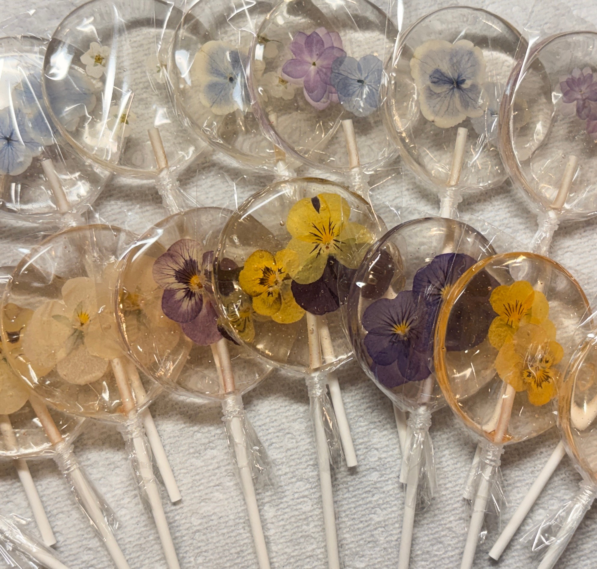 Clear heart-shaped lollipops with colorful pressed flowers inside, arranged on a white surface.
