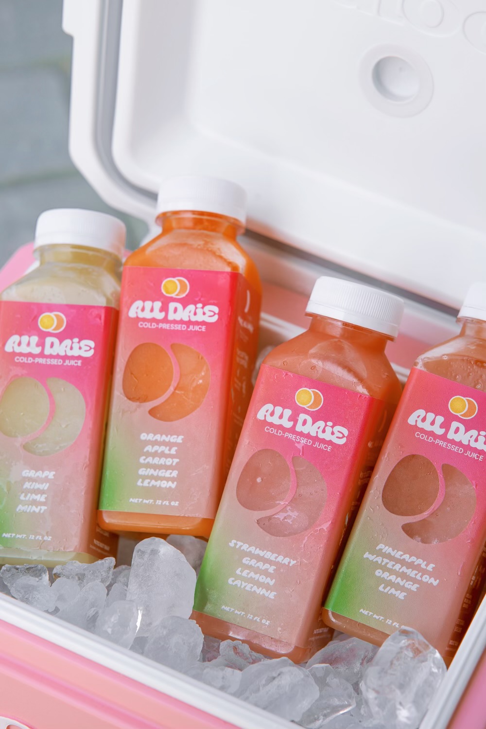 Four bottles of juice in a cooler filled with ice, with a white lid open above them.