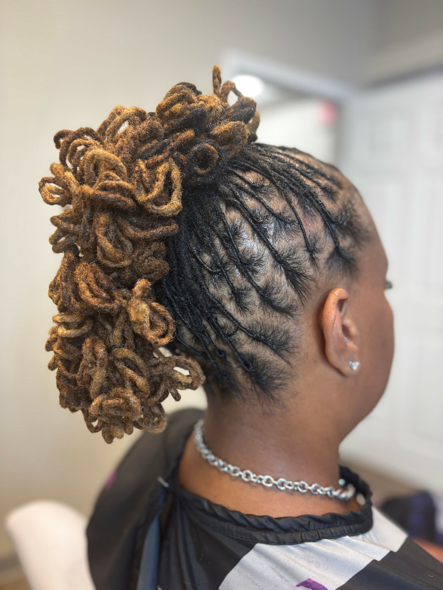 Side view of a woman with styled dreadlocks in a high bun, wearing earrings and a necklace.